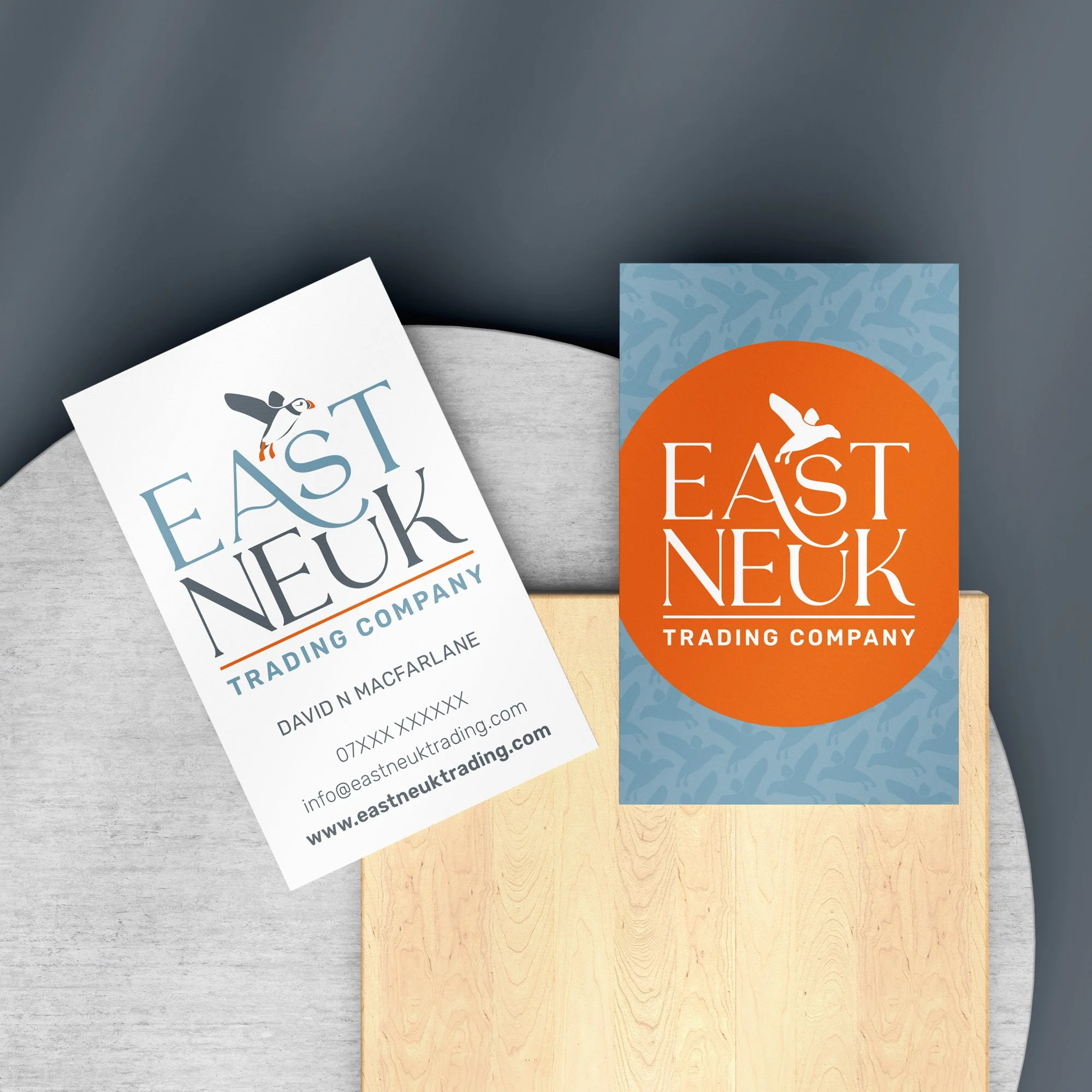 Business cards on a table for East Neuk Trading Company, featuring a bird logo and contact information.