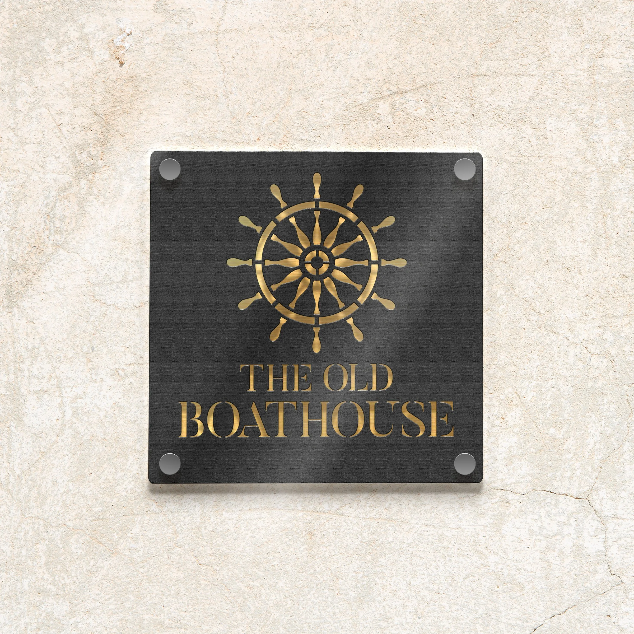 A black metal sign with a ship's wheel design and gold-colored text that reads 'The Old Boathouse', mounted on a beige, textured wall.