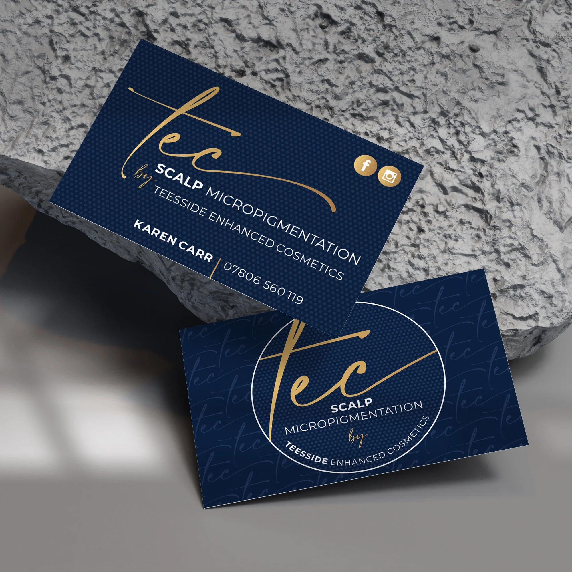 Business cards for Tec Scalp Micropigmentation, featuring a blue background, gold and white text, and social media icons, placed on a textured stone surface.