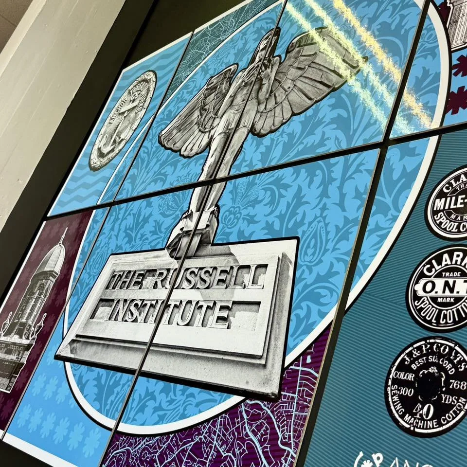 A wall with a mural featuring a gray bird perched on a sign that reads "The Russell Institute," with a blue patterned background. To the left, a part of a tall tower is visible. To the right, there are several vintage-style black and white circular l