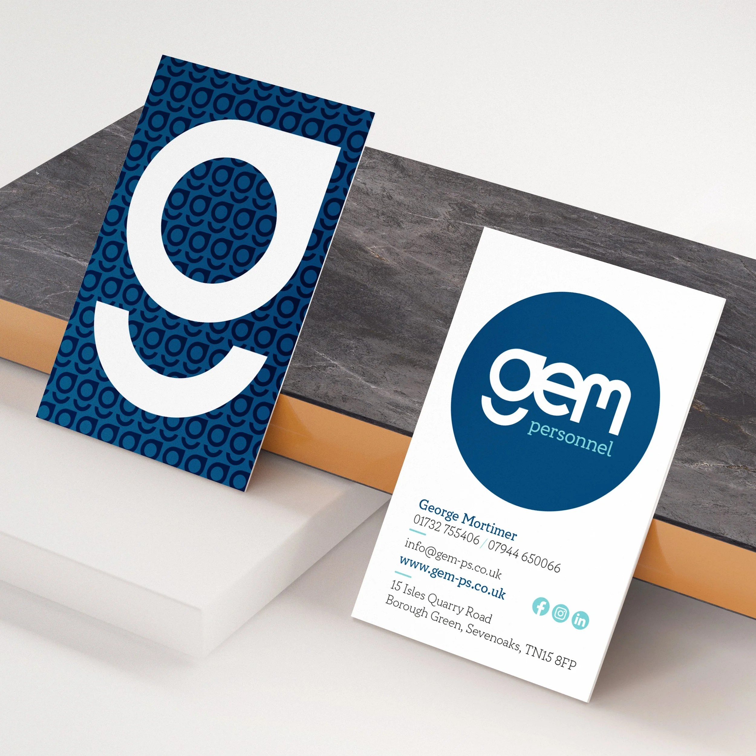 Business card for GEM personnel with contact details and social media icons next to a blue patterned sign with white logo.