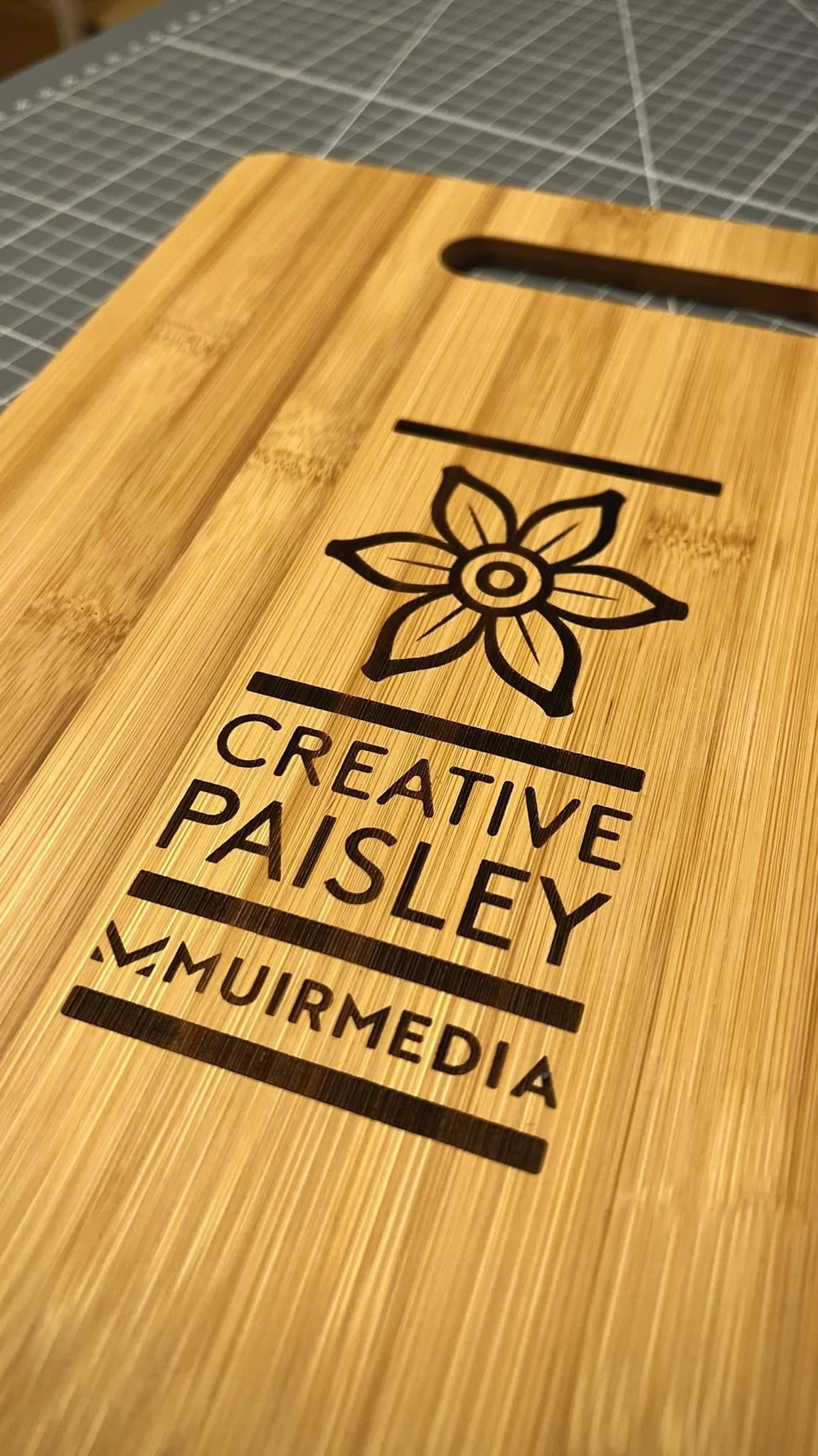 A wooden sign with a flower illustration and the text 'Creative Paisley' and 'V. Muir Media' engraved on it.