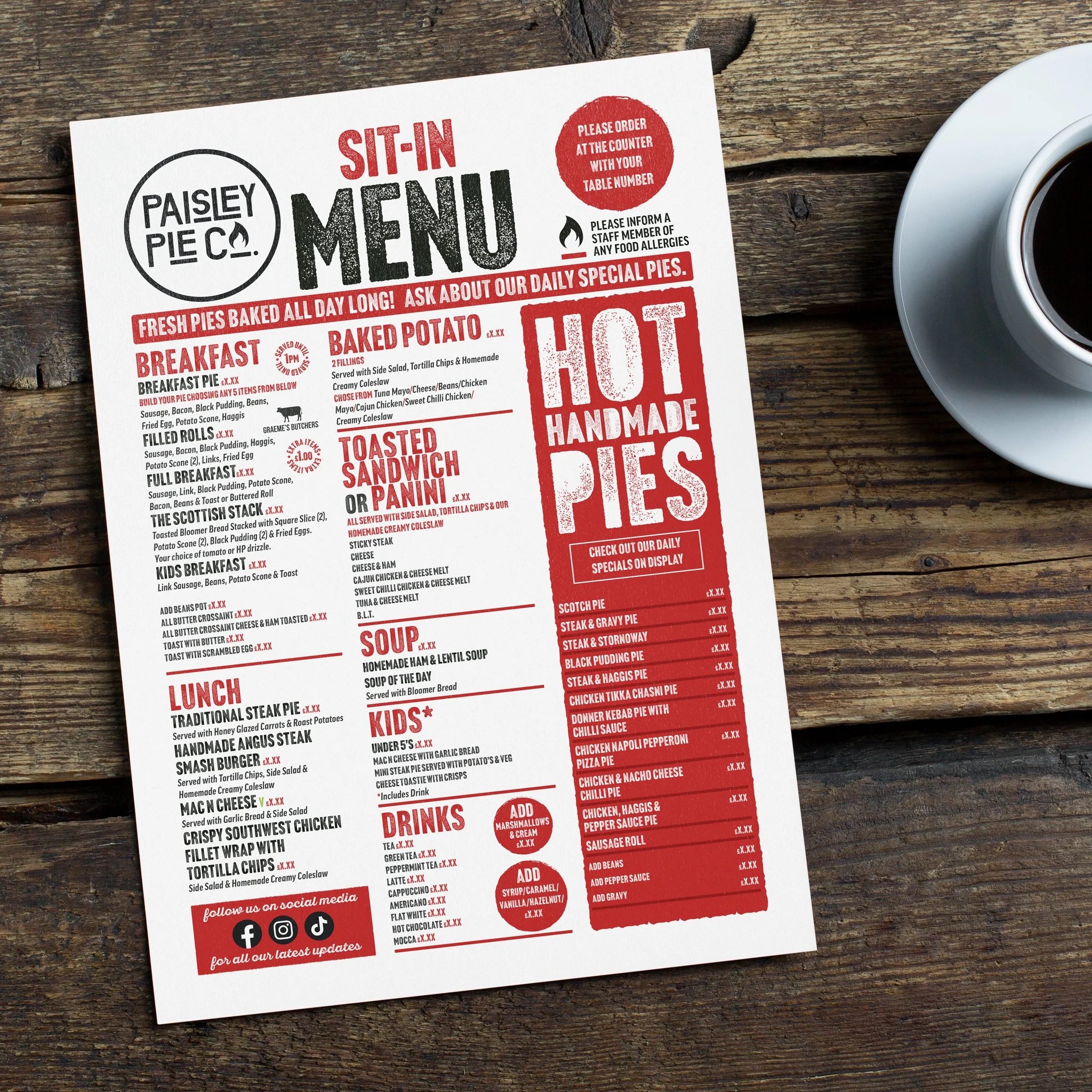 A sit-in menu from Paisley Pie listing items such as breakfast, baked potato, toasted sandwich or panini, soup, kids' meals, drinks, and various handmade pies with daily specials on display. The menu is on a wooden table with a cup of coffee beside i