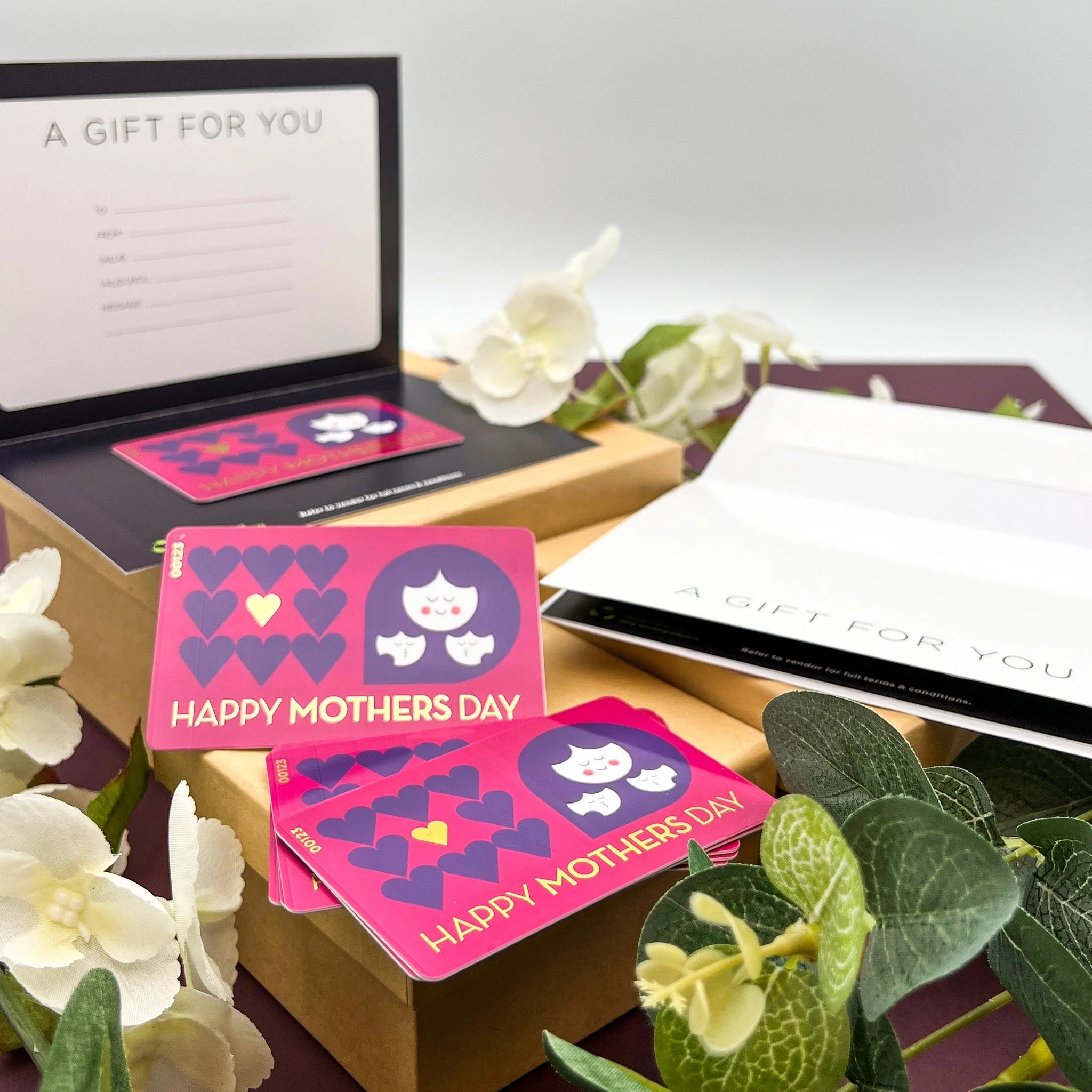 Mother's Day gift set with greeting cards, white flowers, and greenery, with gift envelope and card box in the background.