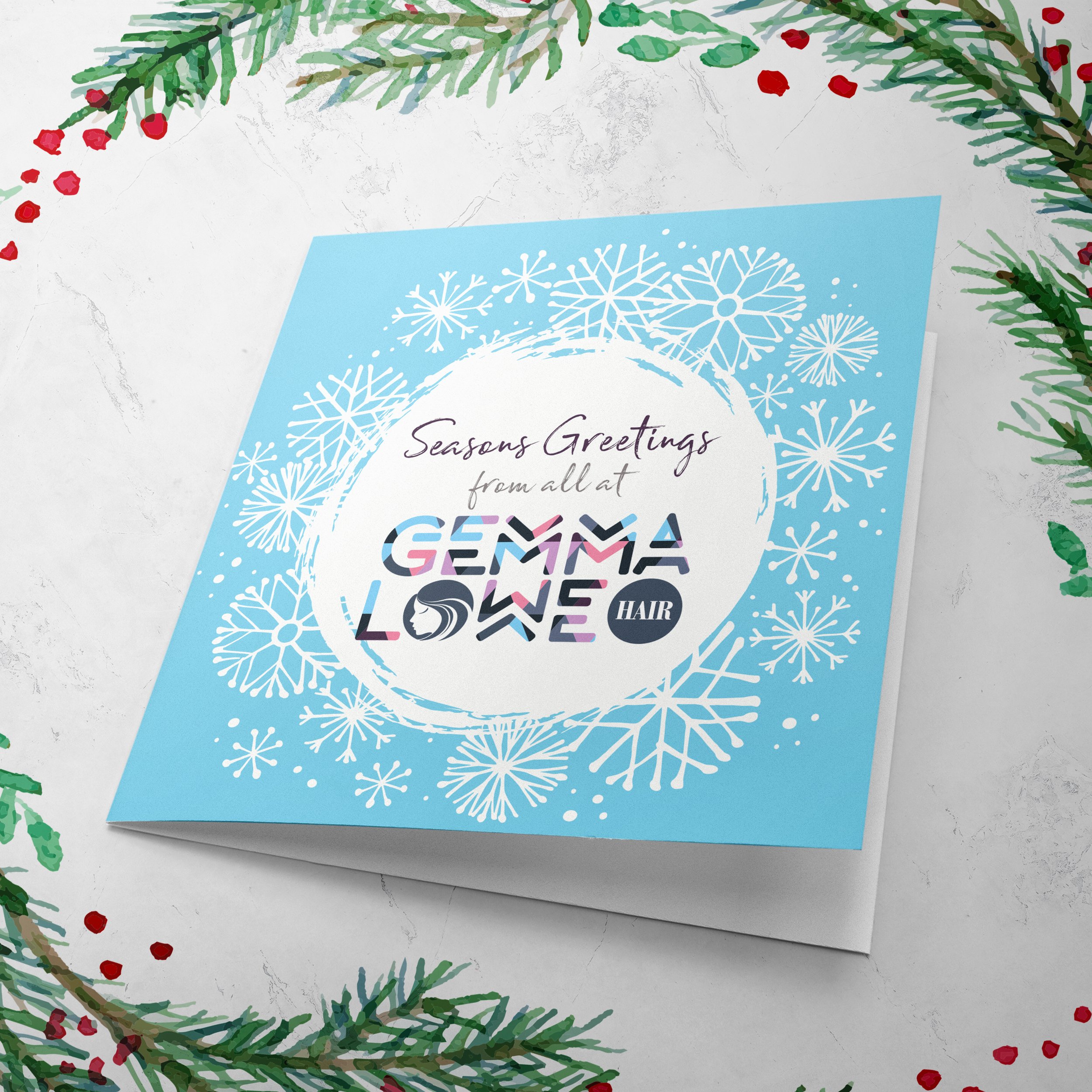 A holiday greeting card with a blue background, white snowflakes, and the text 'Season's Greetings from all at Gemma Love Hair' in decorative fonts, surrounded by green pine branches and red berries.