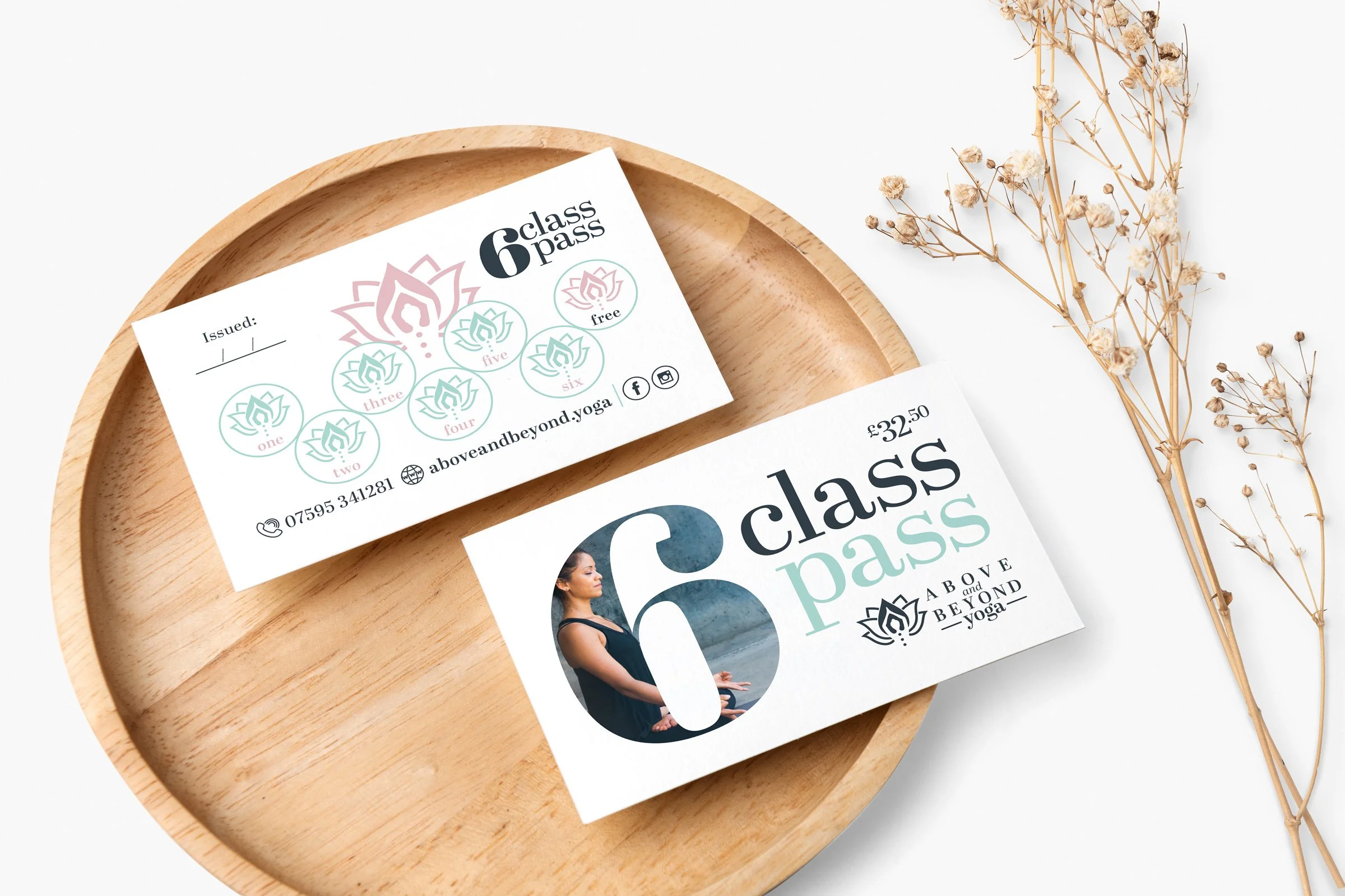 Two yoga class passes on a wooden tray, one with a woman meditating and the other with a lotus flower design and a six-class pass outline, with dried flowers nearby.