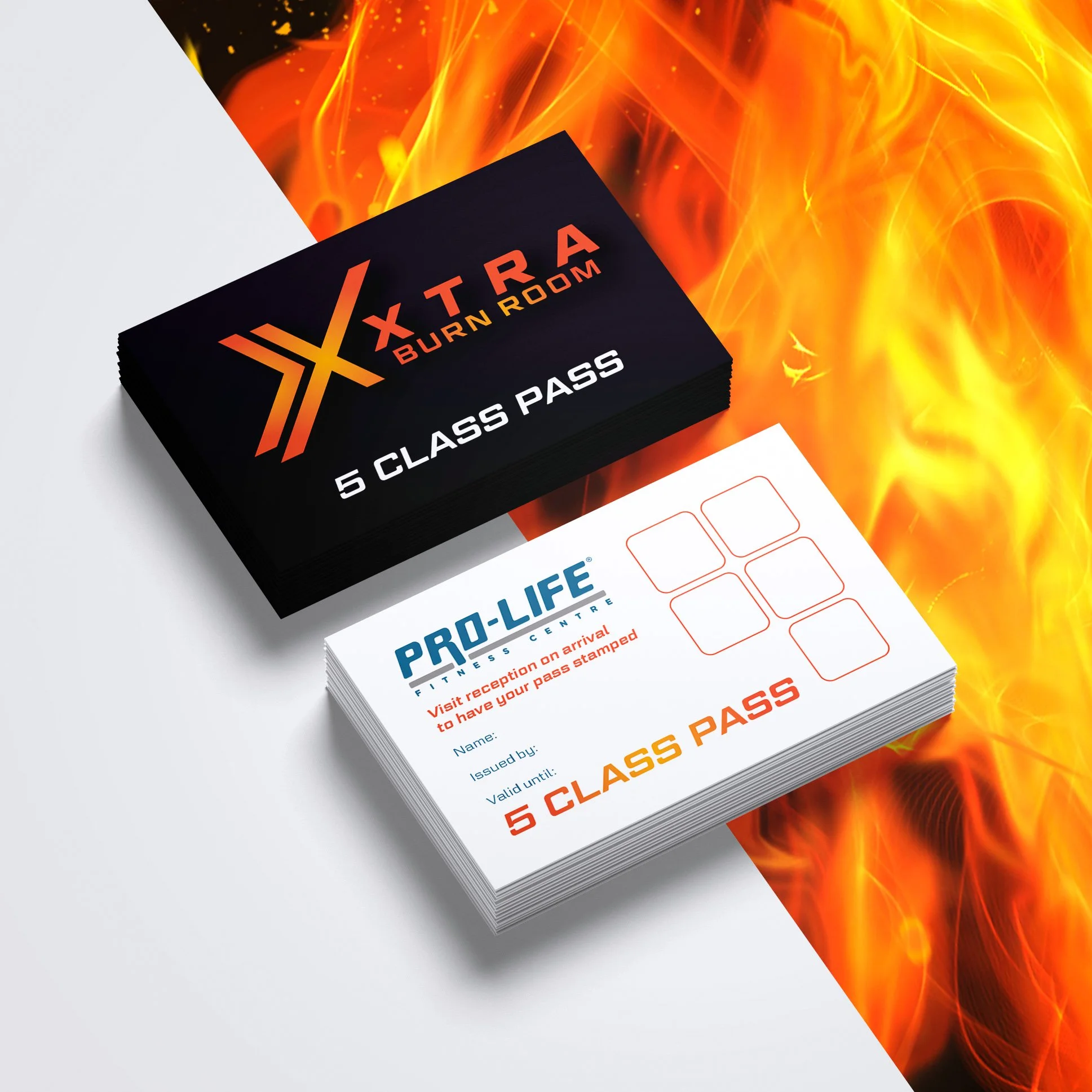Stacks of black and white Pass cards for a gym and a burn room, placed on a surface with a background of flames.
