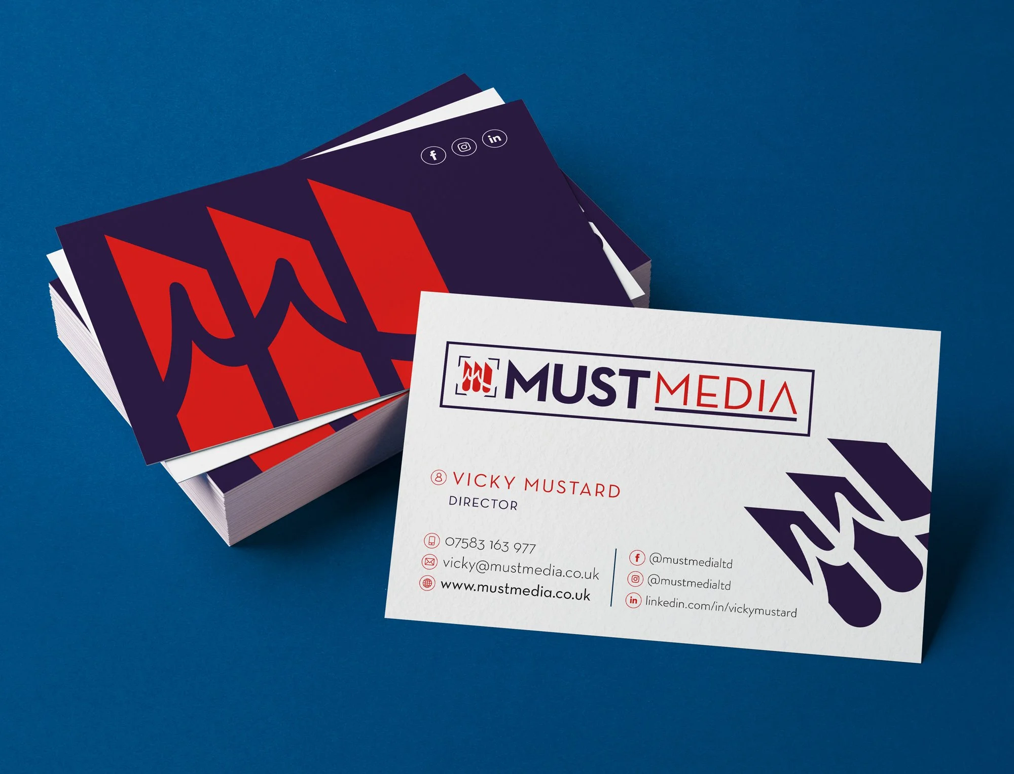 Stack of business cards for Must Media, with one card displayed showing contact information for Vicky Mustard, including phone, email, website, and social media handles, on a blue background.