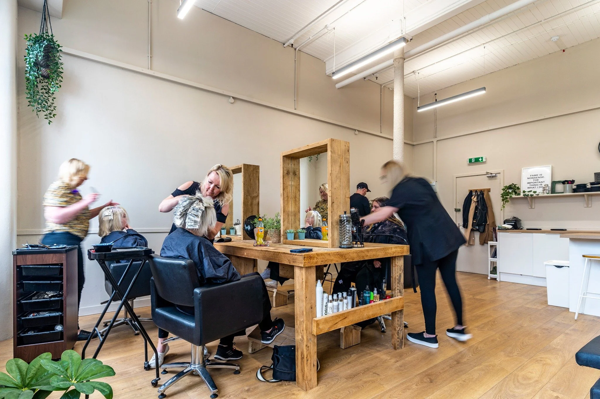 People getting haircuts in a modern salon with wooden furniture, mirrors, and natural decor.