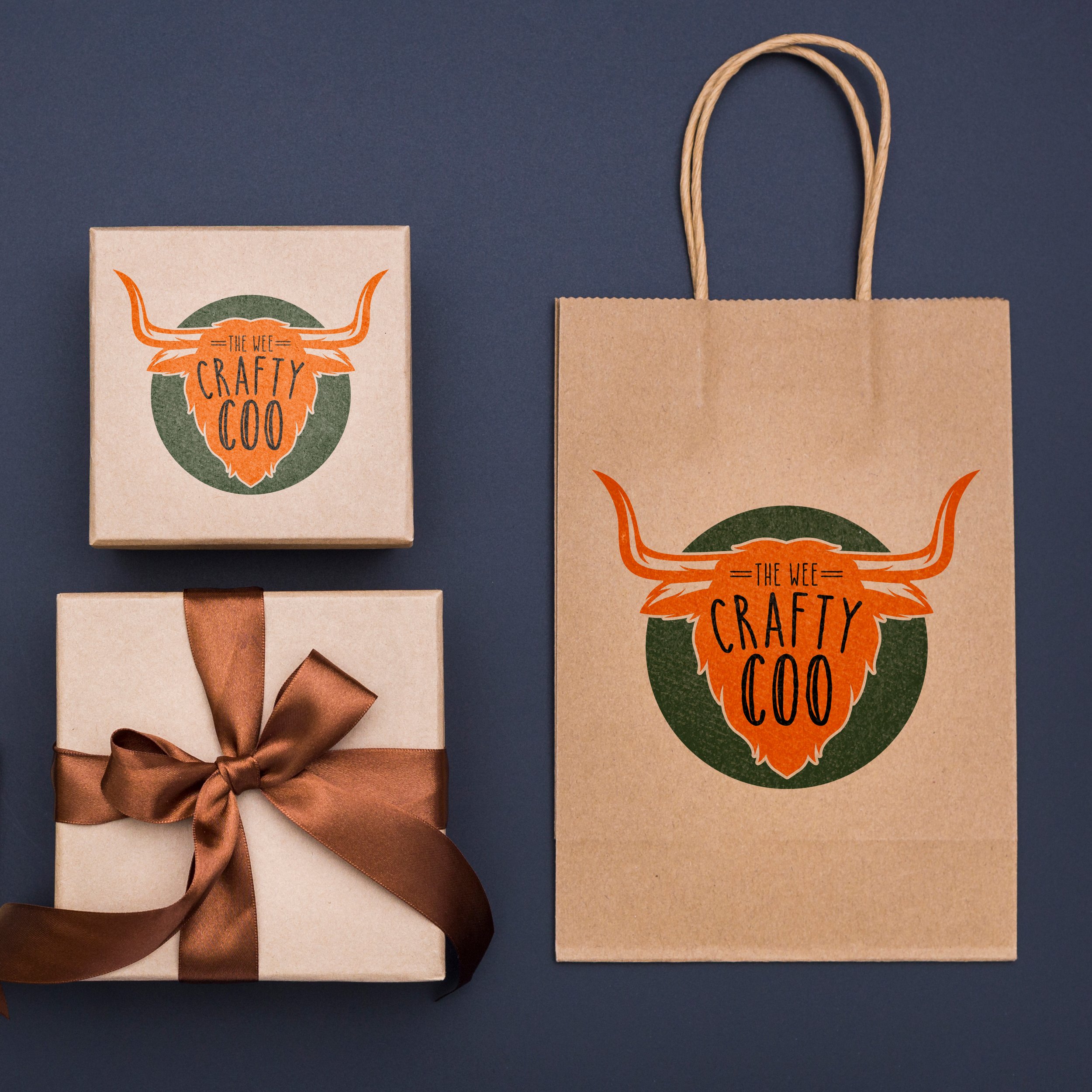 Two gift boxes and a shopping bag with a logo that reads 'The Wee Crafty Coo' featuring a stylized highland cow head with long horns and orange fur, against a blue background.