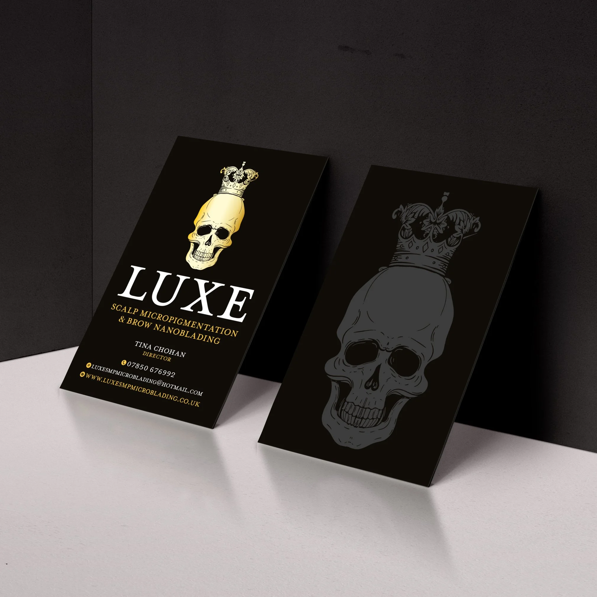 Business cards with skull and crown design, one card with detailed text for a scalp micropigmentation and brow nanoblading service, black background, on a white and black surface.