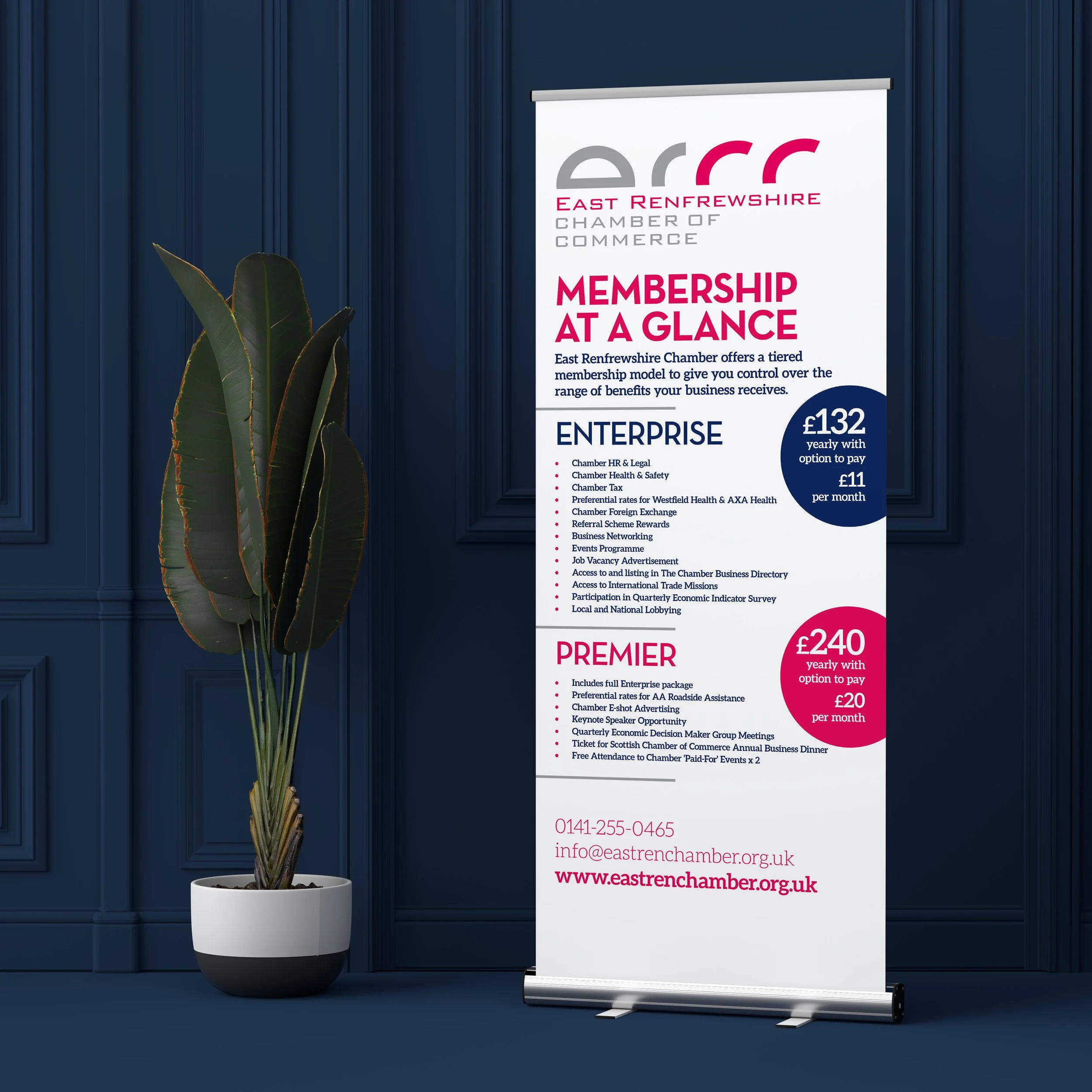 Information stand with details about East Renfrewshire Chamber of Commerce membership, listing prices, benefits, and contact information on a blue wall background beside a potted plant.