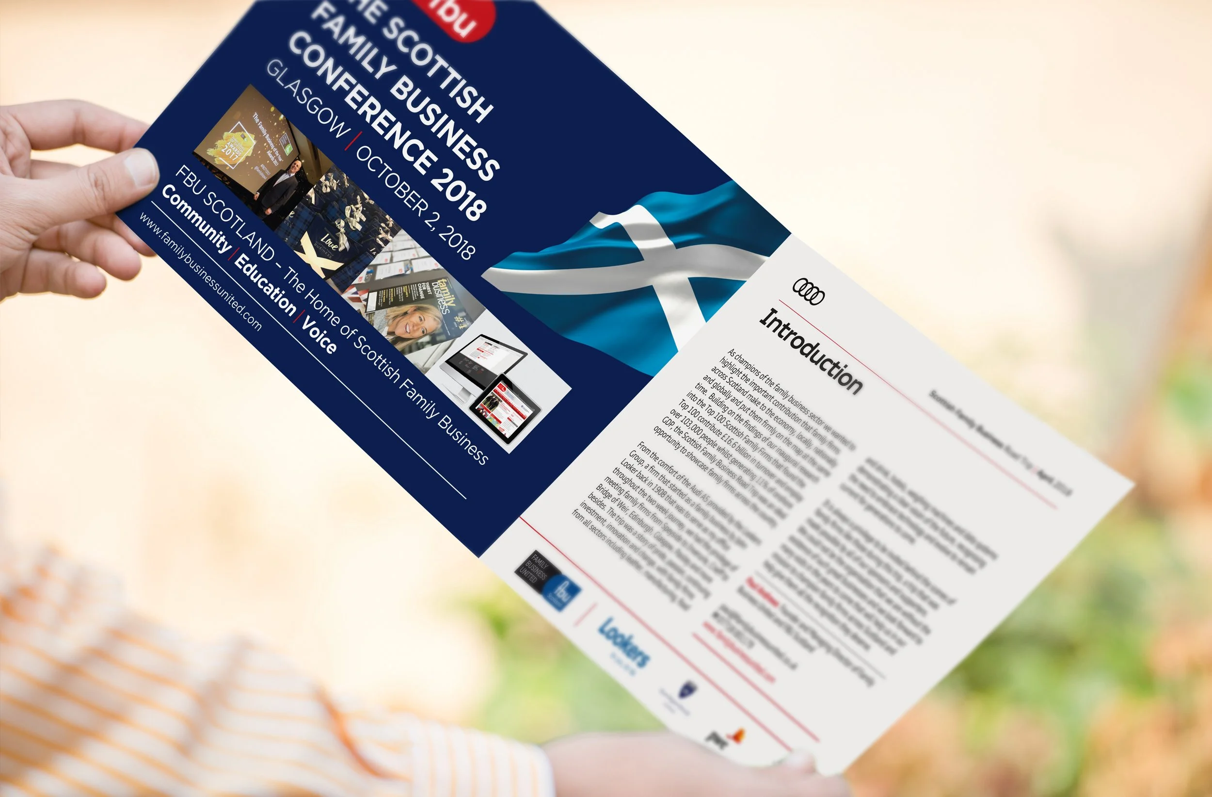 A person holding a flyer for the Scottish Family Business Conference 2018, which took place in Glasgow on October 2, 2018. The flyer features a Scottish flag and information about the event.