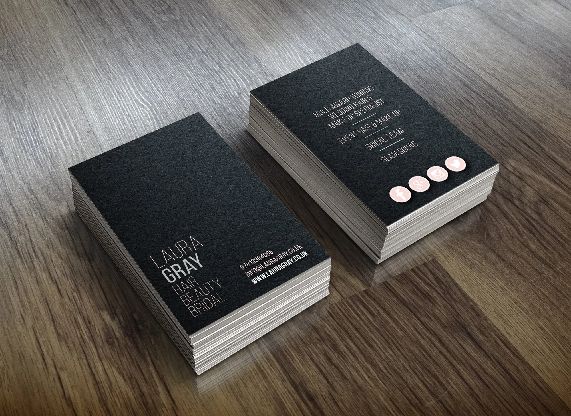 Stack of black business cards for Laura Gray, a hair, beauty, and bridal specialist. Contact info and website are included on the cards. The cards are on a wooden surface.