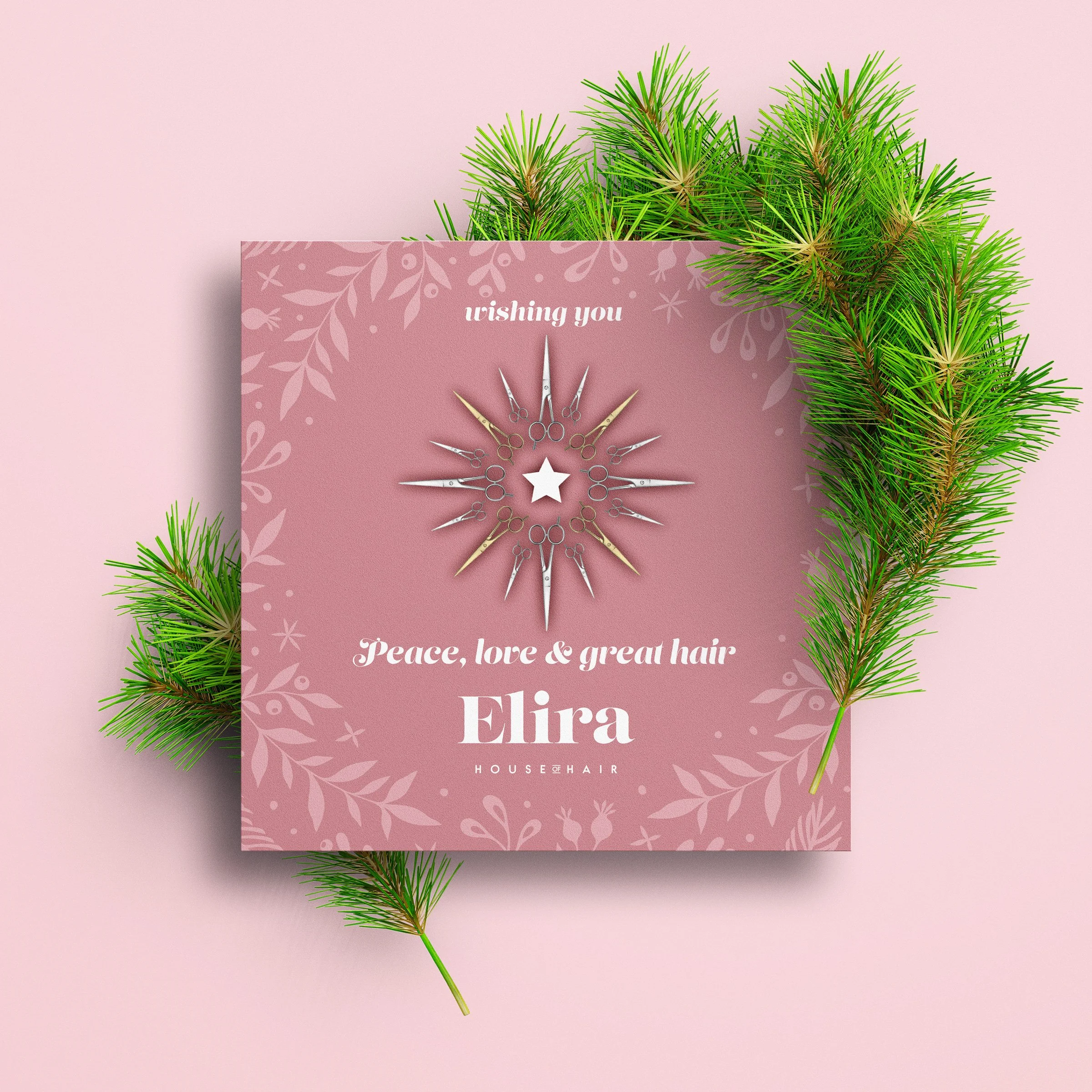 A pink gift box with a message, surrounded by pine branches, that says 'wishing you Peace, love & great hair Elira' and features a star-shaped hair tool in the center.