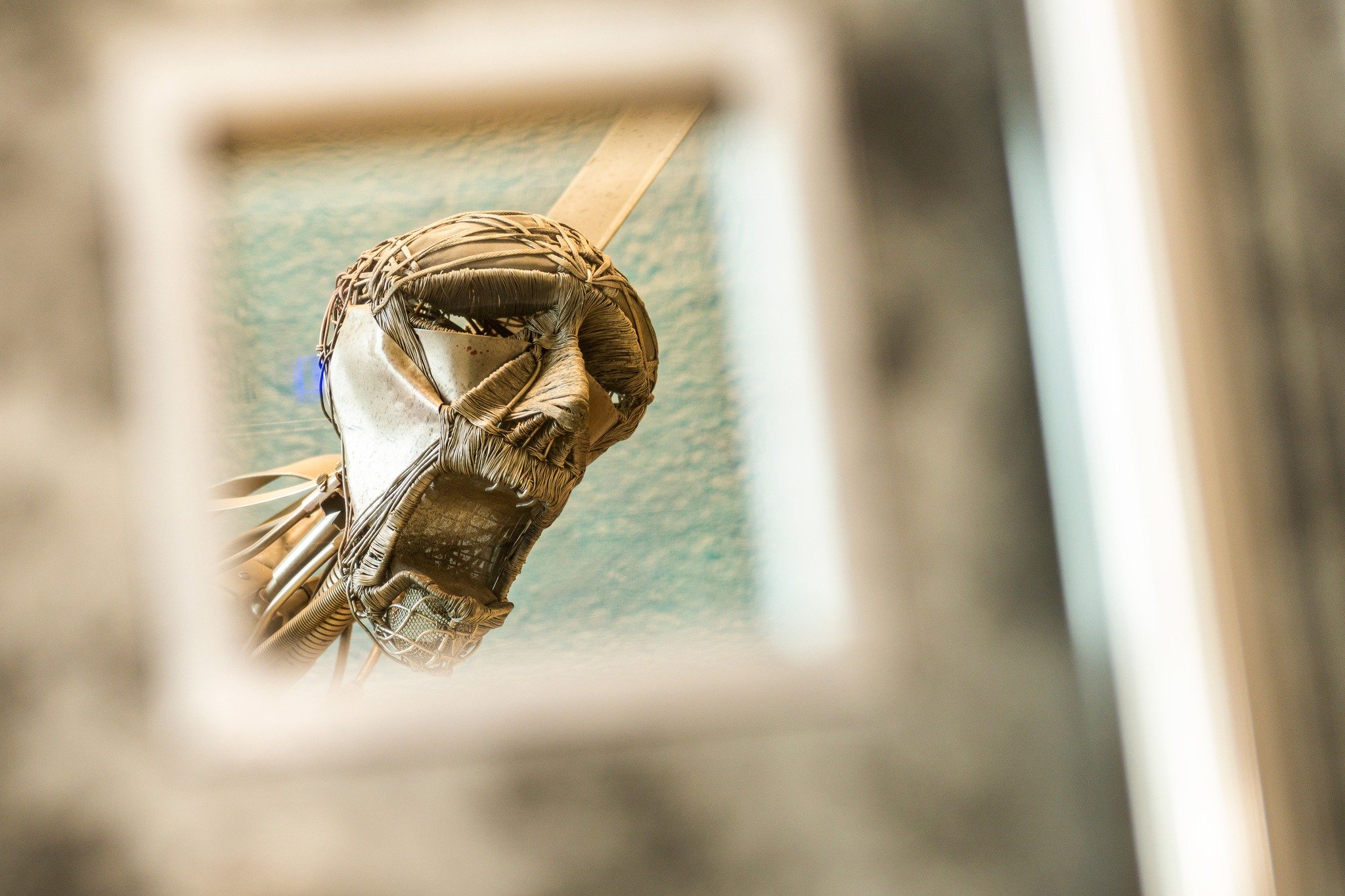 A wicker beach chair with a canopy, viewed through a narrow opening, with a blue ocean and sky in the background.