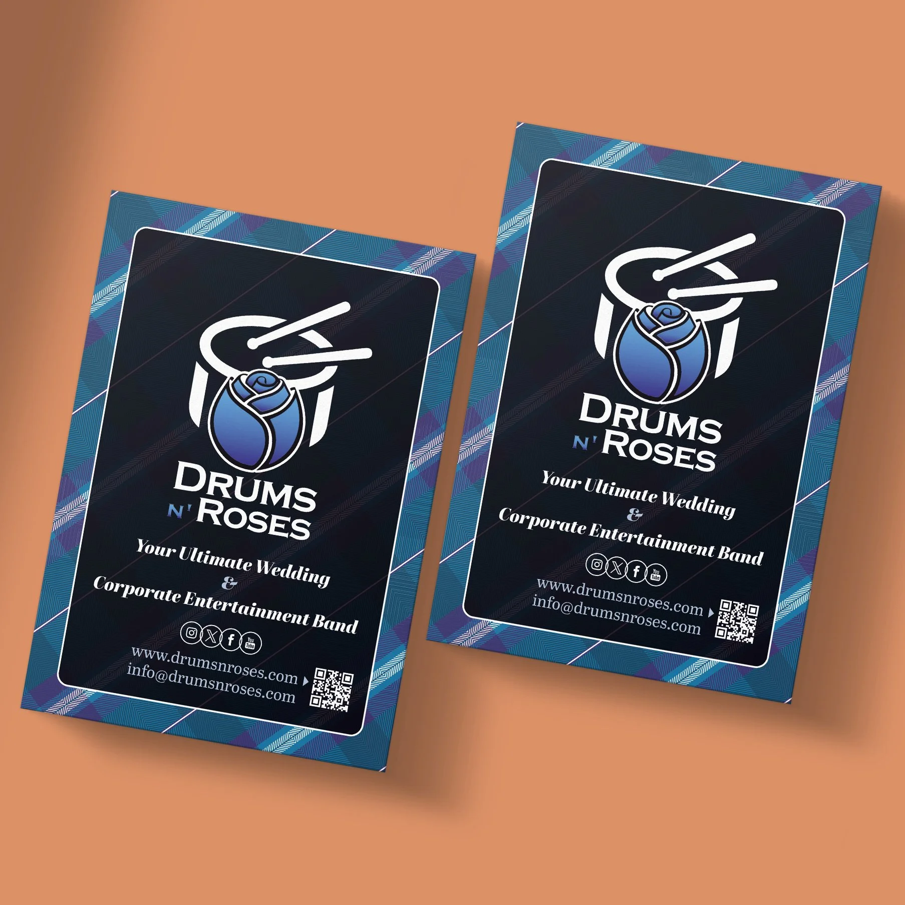 Two business cards for Drums N Roses, a wedding and corporate entertainment band. The cards have a dark background with a blue and plaid border, and include a logo of a rose with drumsticks, the band name, contact information, and social media icons.