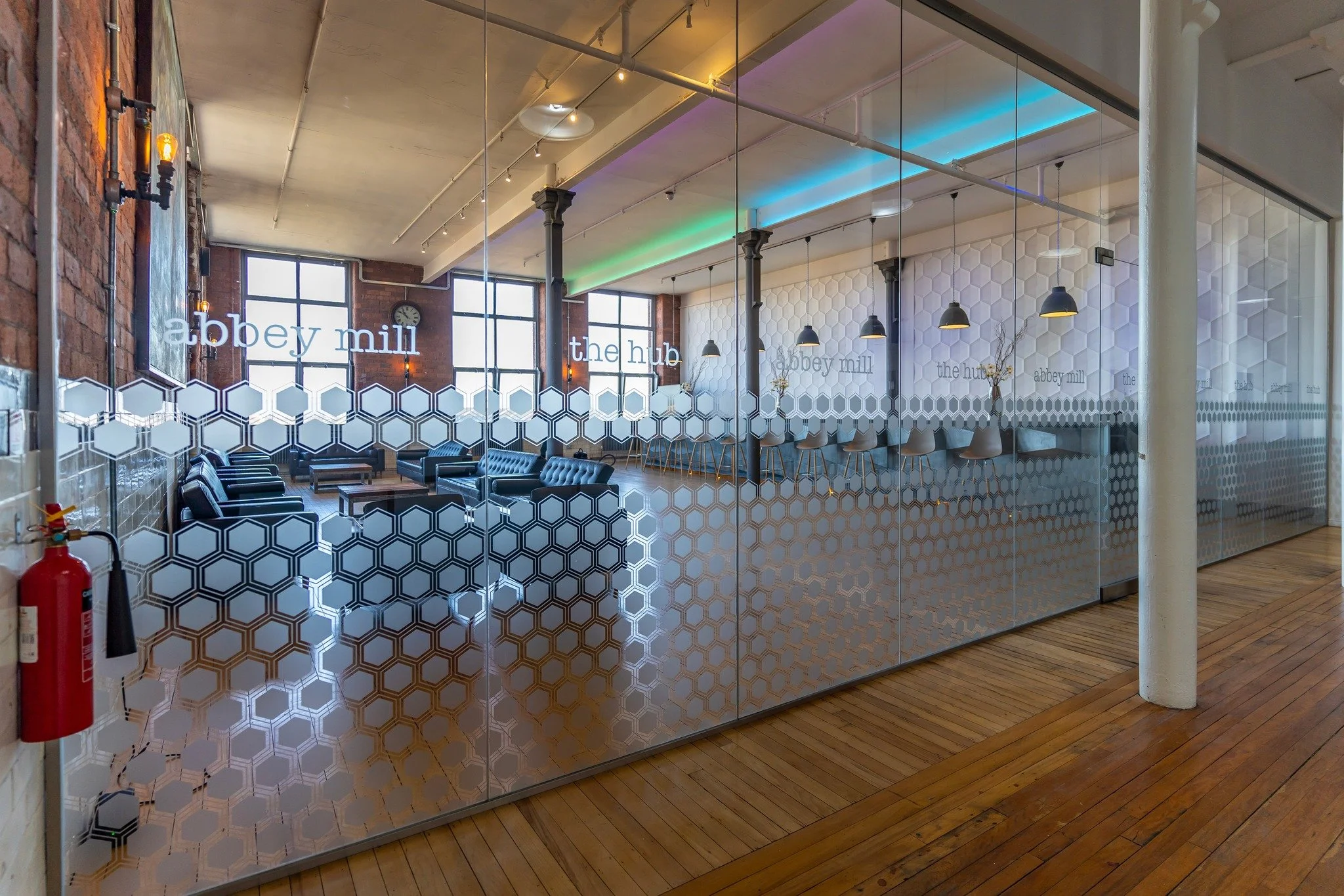 Interior of a modern lounge or workspace area with glass walls, black leather seating, and large windows with industrial design elements.