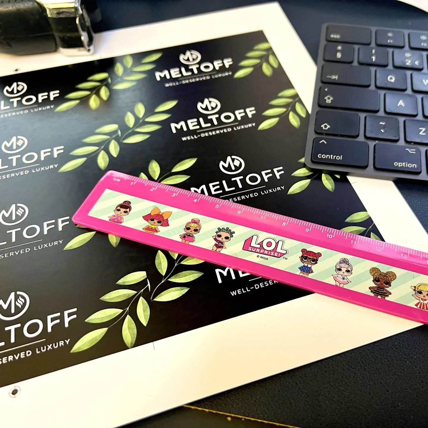 Desk with Meltoff branded paper, a pink LOL Surprise ruler, a partial keyboard, and a black stapler.