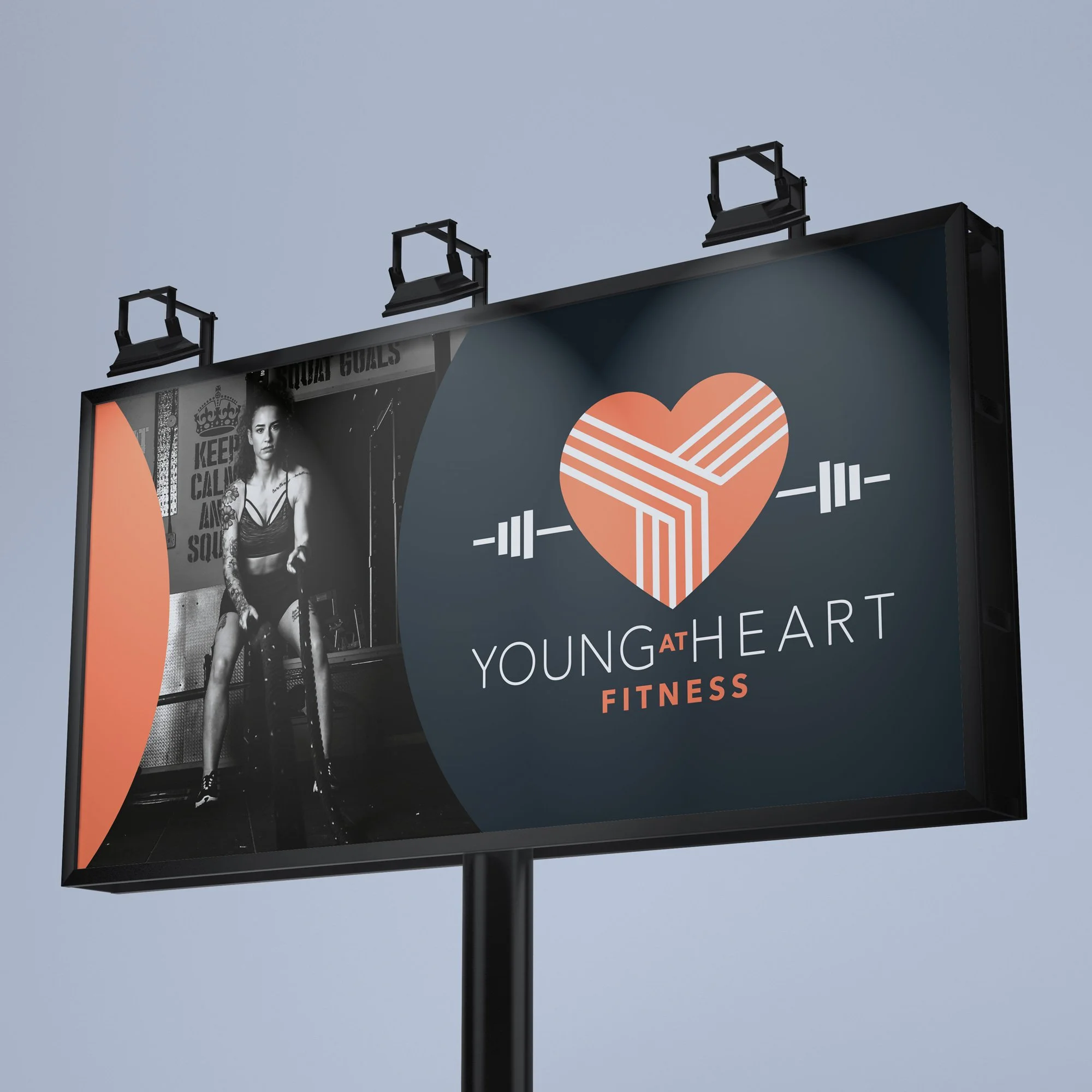 Billboard with a logo of a heart with diagonal lines and barbell, and text 'Young at Heart Fitness'. A black-and-white photo of a woman with tattoos lifting weights is on the left side of the billboard.