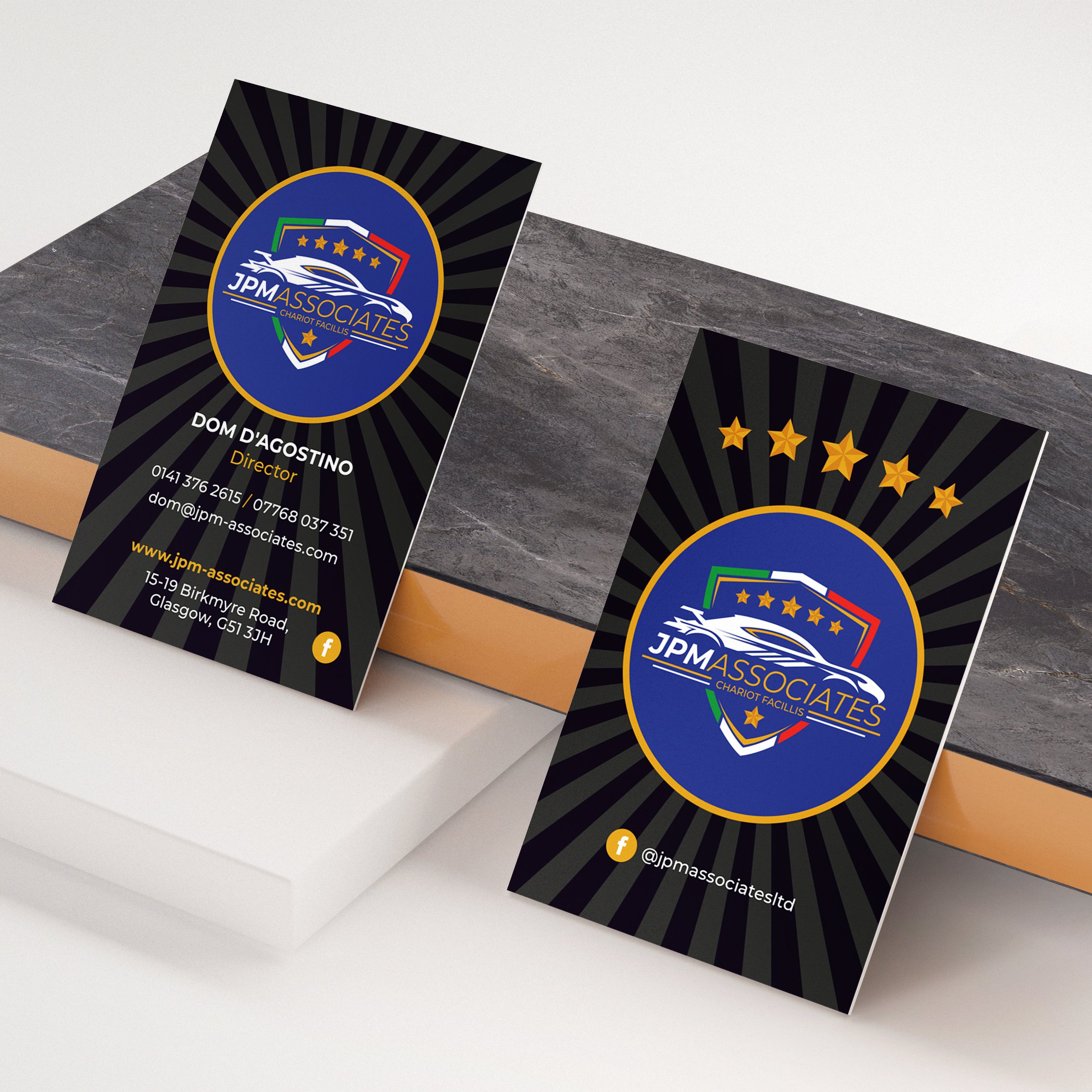 Business card for JPM Associates featuring a logo with a car and a shield, with gold stars above. The front displays contact information including the name Dom D'agostino, title of director, phone numbers, email, website, and address. The back shows 