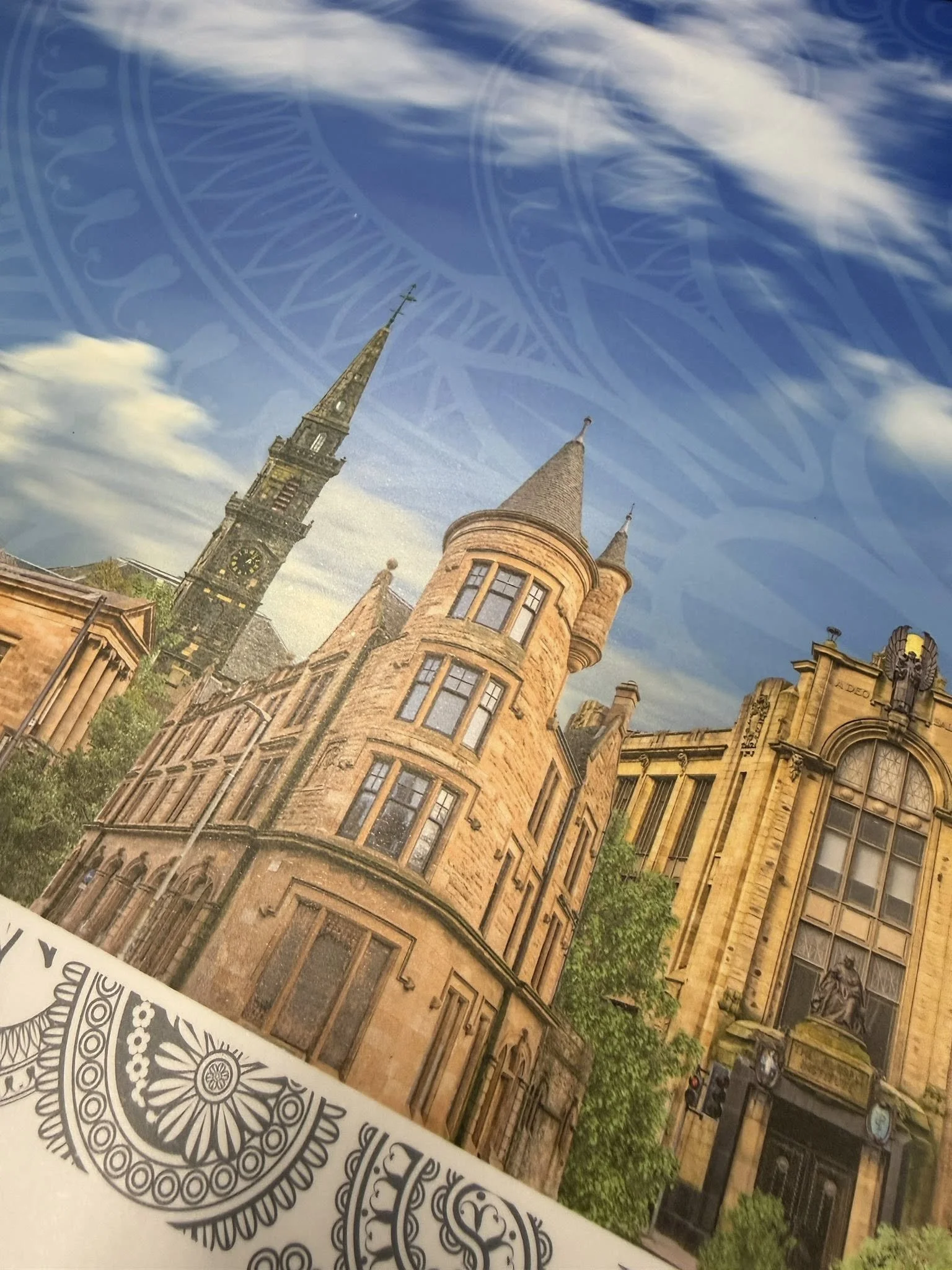 A photograph of historic buildings including a church with a tall clock tower and spires, and another yellow gothic-style building with detailed facades, with a blue sky and clouds in the background.