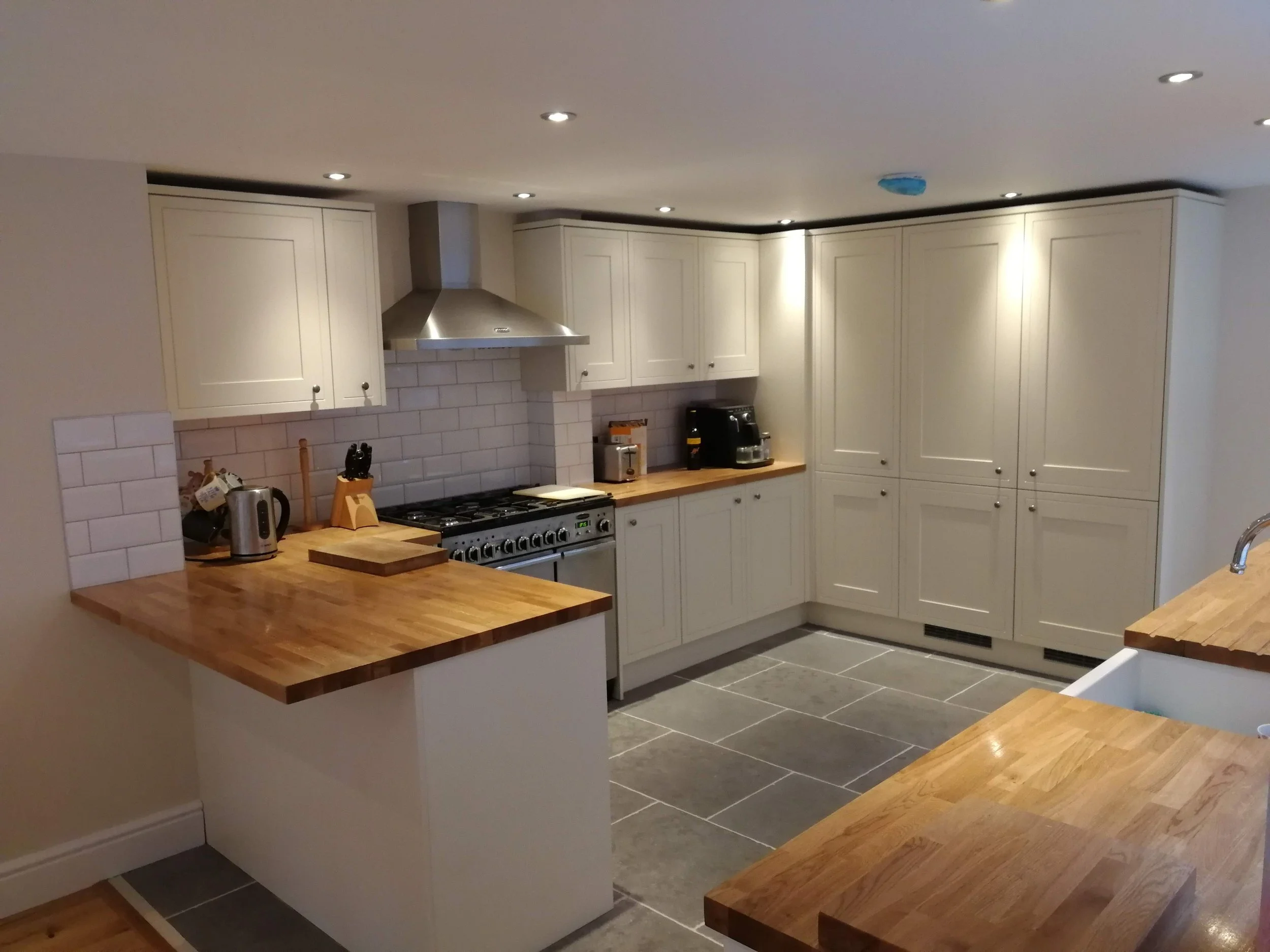 Modern kitchen with a white island, beige bar stool, and overhead rustic beams. Decor includes a floral arrangement, cup, and books, creating a cozy ambiance.
