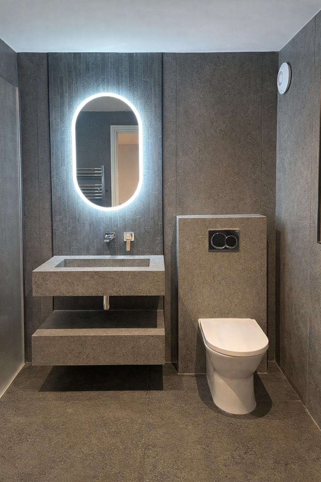 A modern bathroom sink with a rectangular, stone-textured basin is lit by an oval mirror with LED lights. A red line runs horizontally across the image.