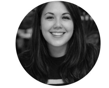 A black and white portrait of a woman smiling warmly at the camera, with long dark hair, set against a blurred interior background. The tone is friendly and inviting.