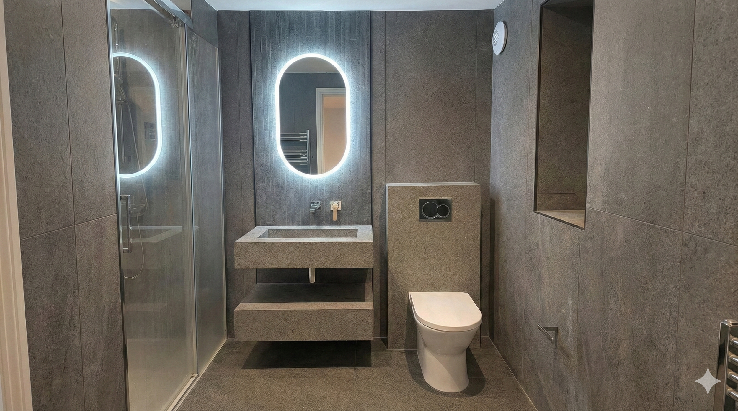 Modern bathroom with dark stone textures. An oval mirror with LED backlight is above a sleek rectangular sink. A toilet is to the right, creating a minimalist, clean atmosphere.
