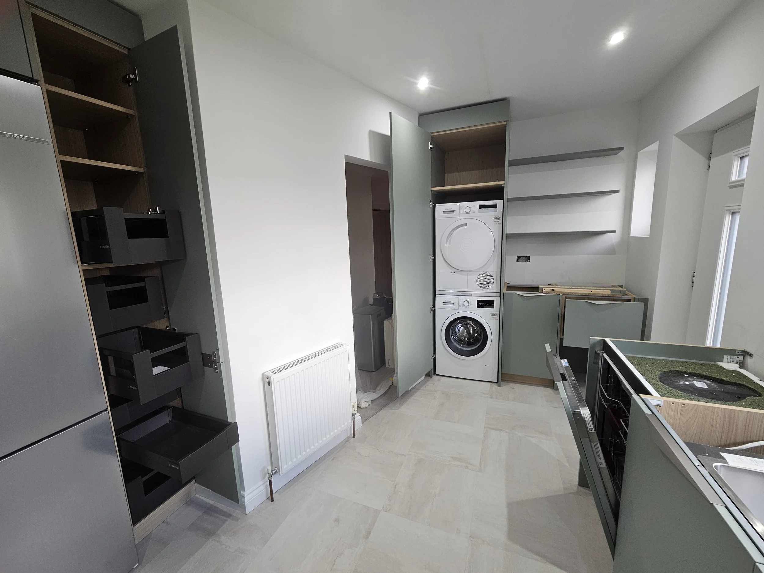 Bright laundry room with teal cabinets, floating shelves, and a stacked washer and dryer. Open shelves and a cozy, organized feel.