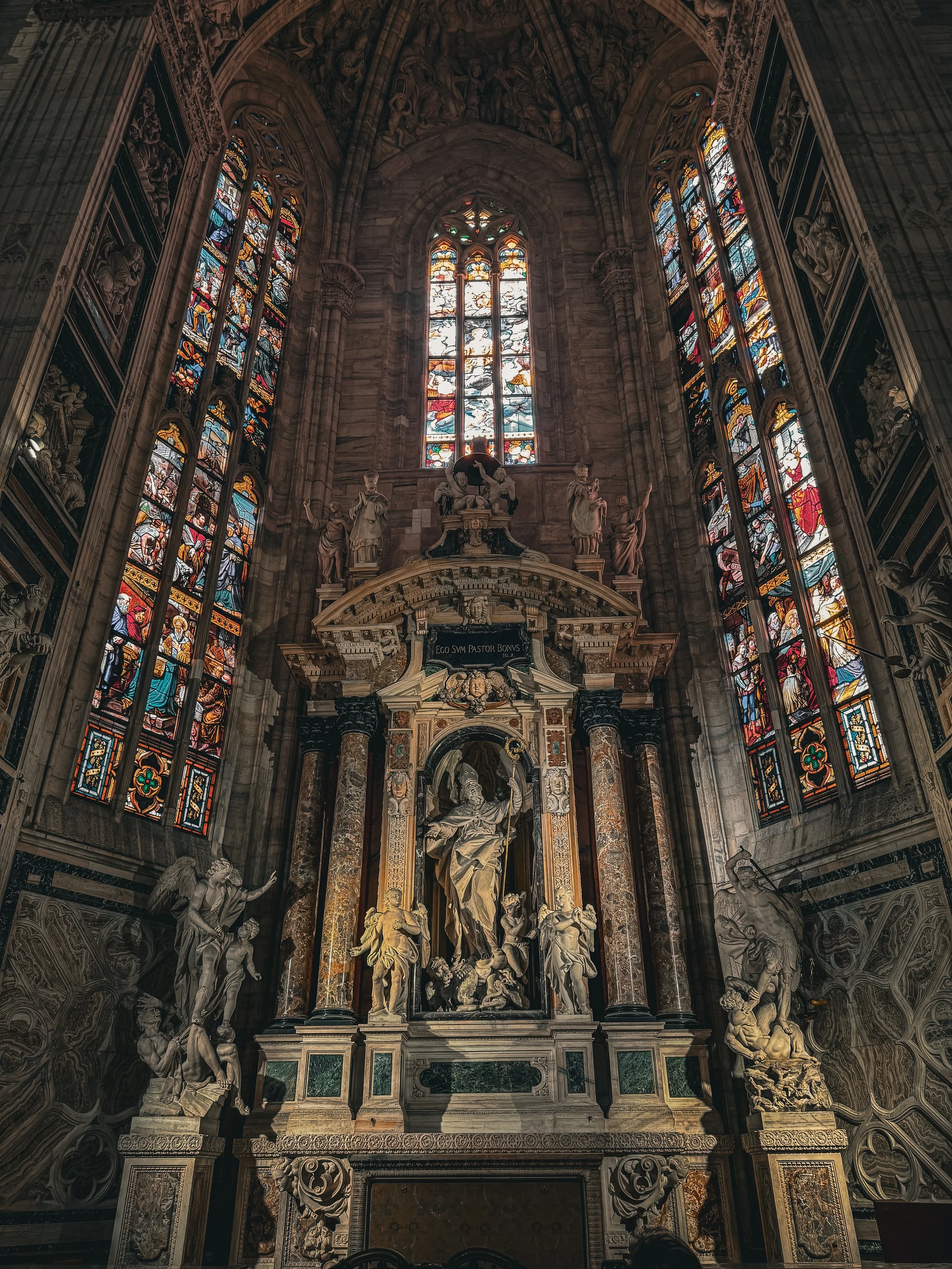 Interior of a grand church or cathedral with stained glass windows and intricate statues and sculptures around the altar.