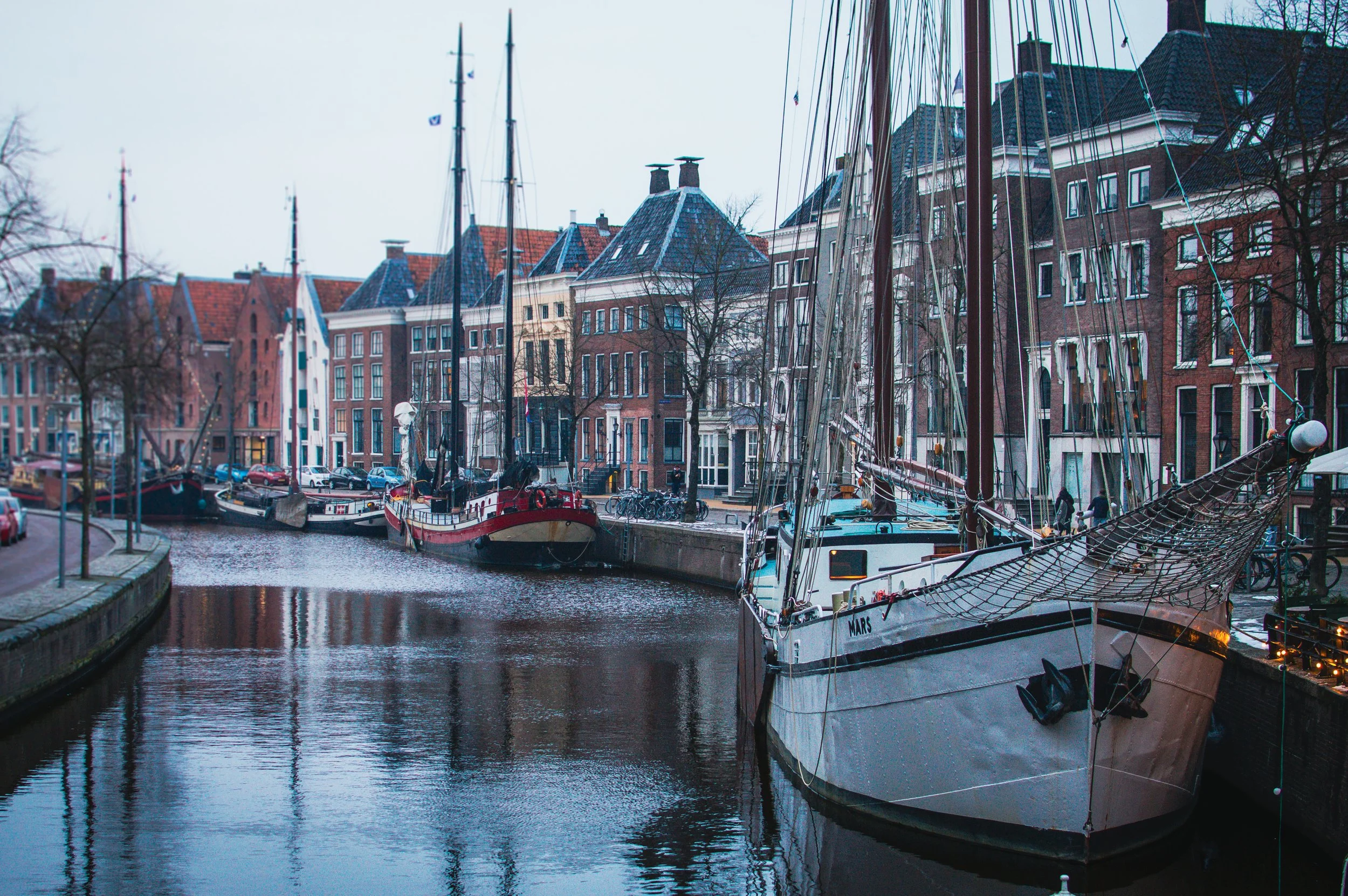 Boats docked along a canal with historic brick buildings lining the waterfront in a city scene.