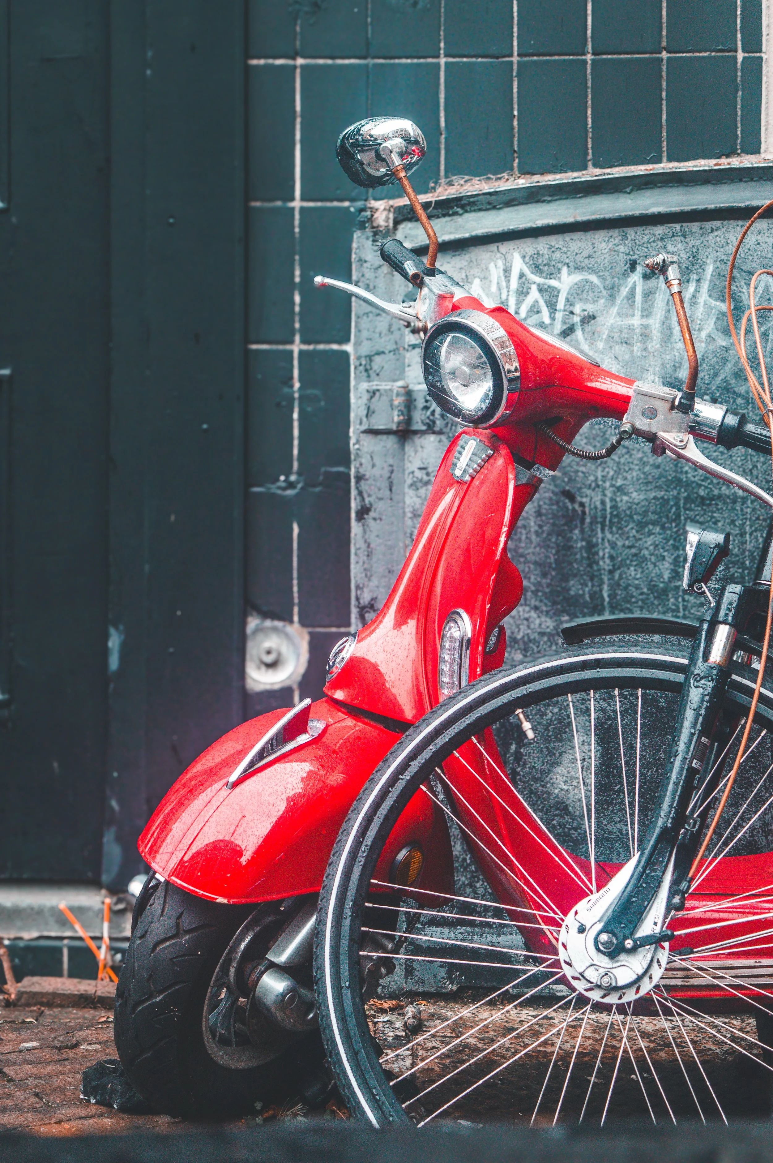 Red vintage scooter and a bicycle parked against a graffiti-covered wall.