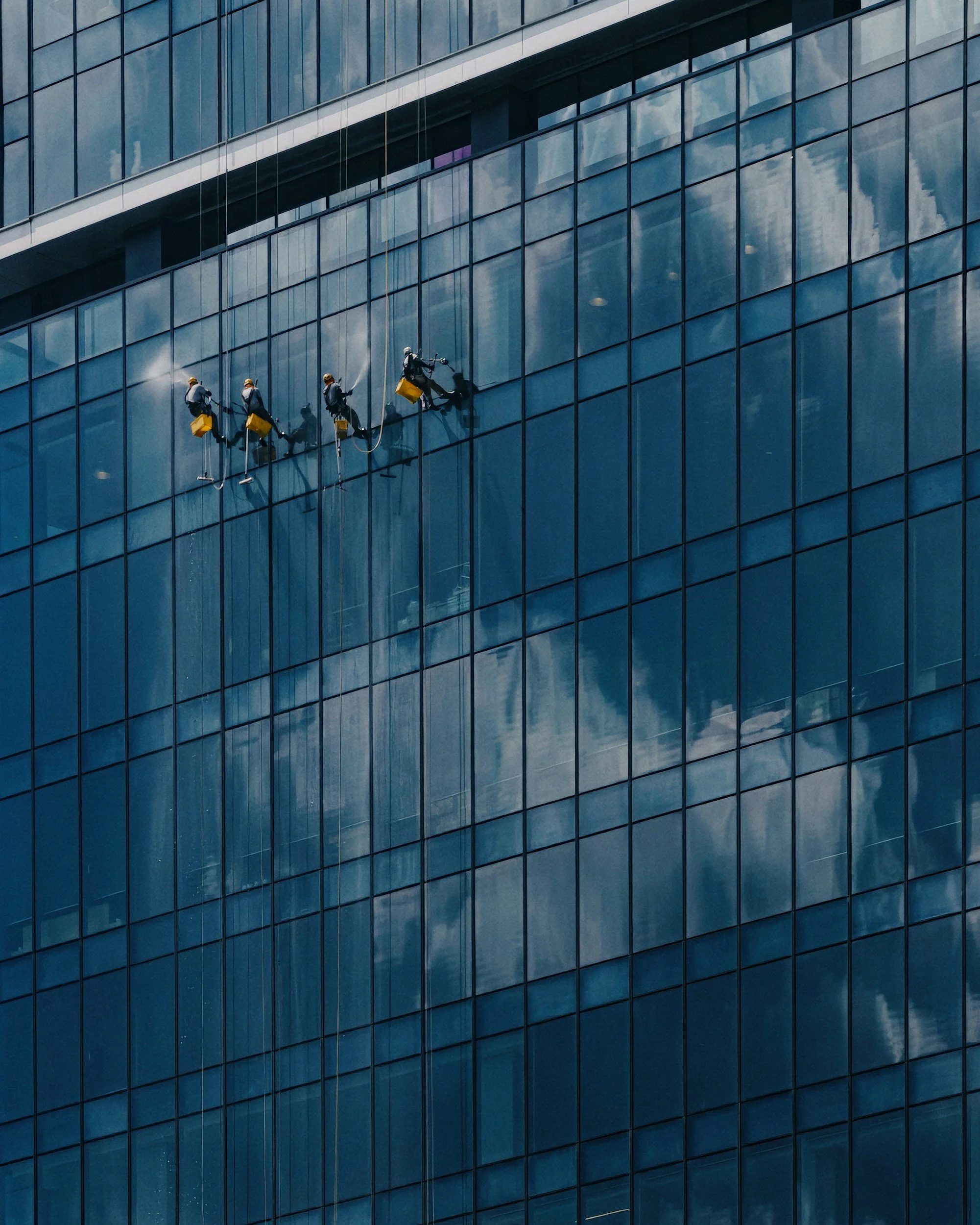 Three window washers cleaning the glass of a modern high-rise building.