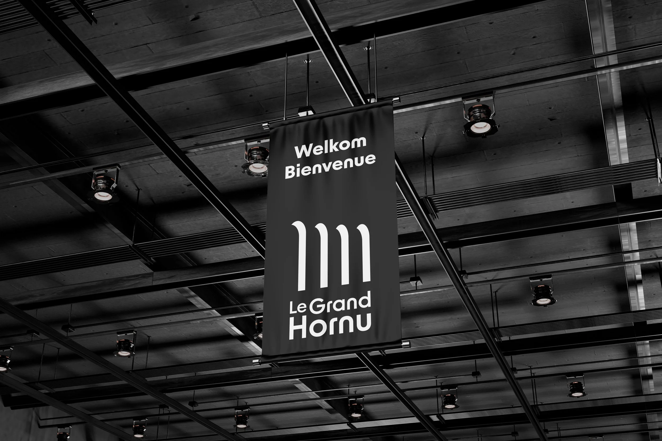 «Signalétique intérieure suspendue au Grand-Hornu : panneau de bienvenue "Welkom Bienvenue" en noir et blanc. Design graphique et wayfinding pour site classé UNESCO par Bower Studio.