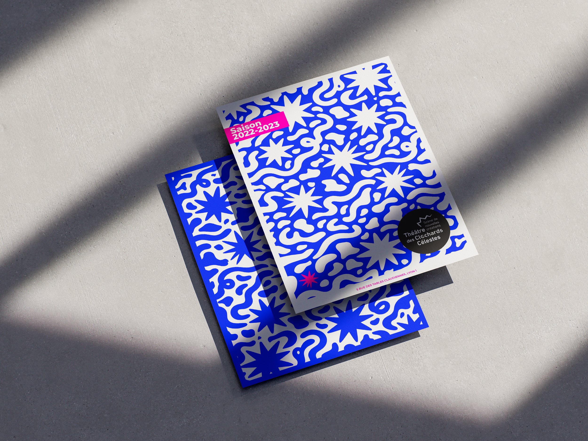 Duo de brochures de saison aux motifs stellaires bleus et blancs, présentées en superposition sur un fond clair texturé.