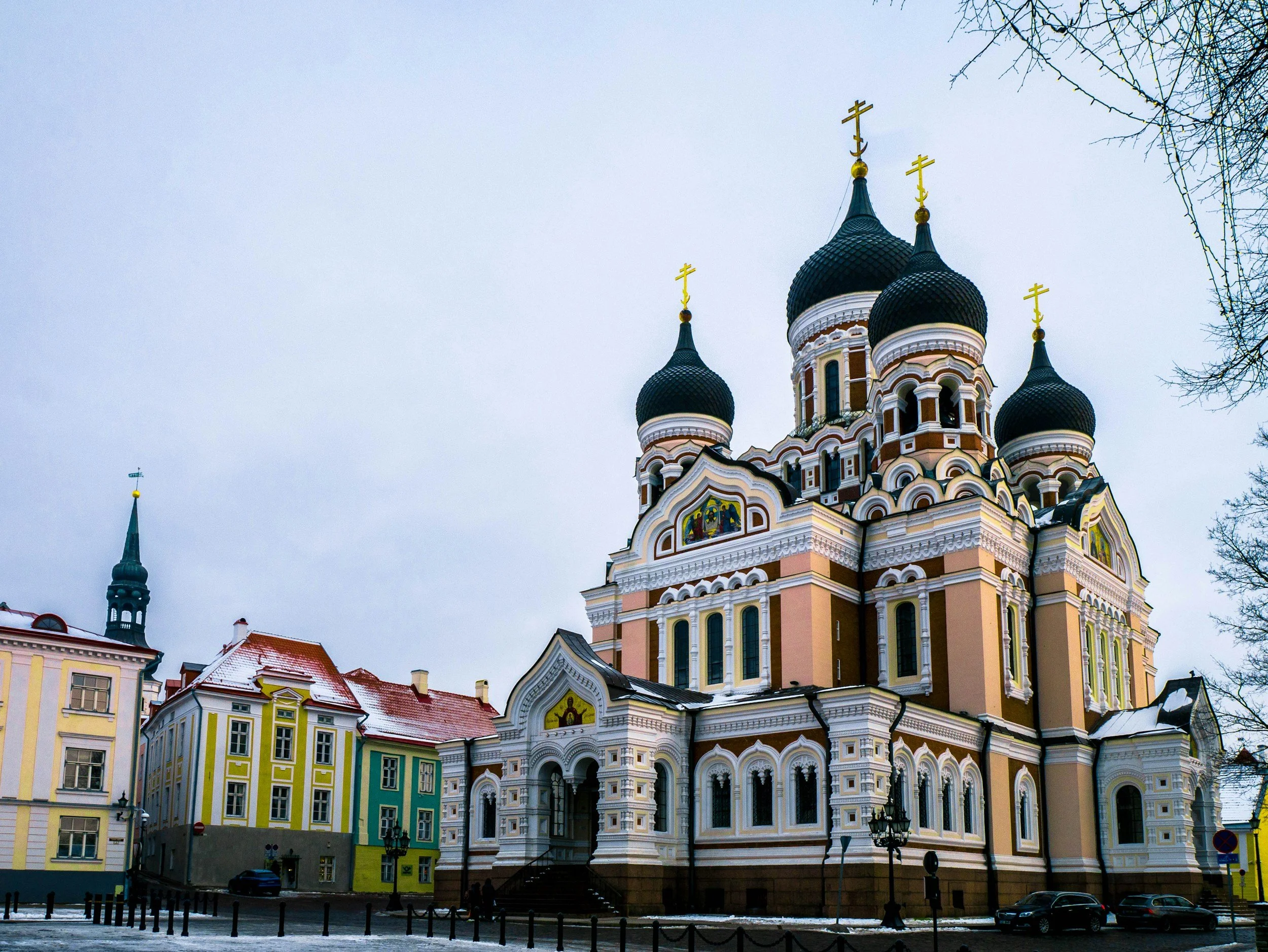 Colorful Eastern Orthodox church with black onion domes and gold crosses, situated in a snowy city square.