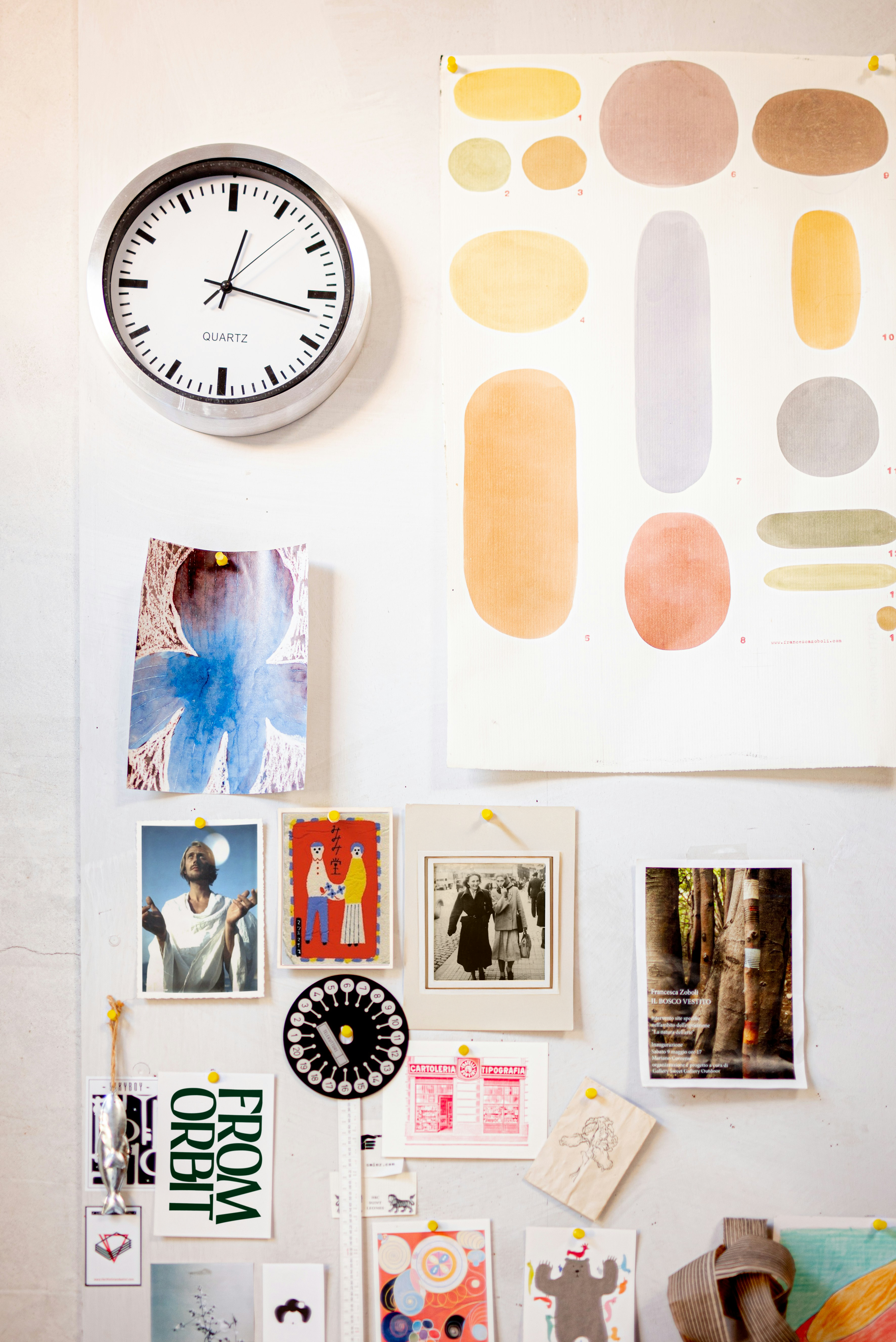 Exploration créative avec un horloge murale, un poster avec des formes de peinture en aquarelle, et diverses photos, illustrations et notes pinées sur un tableau blanc.