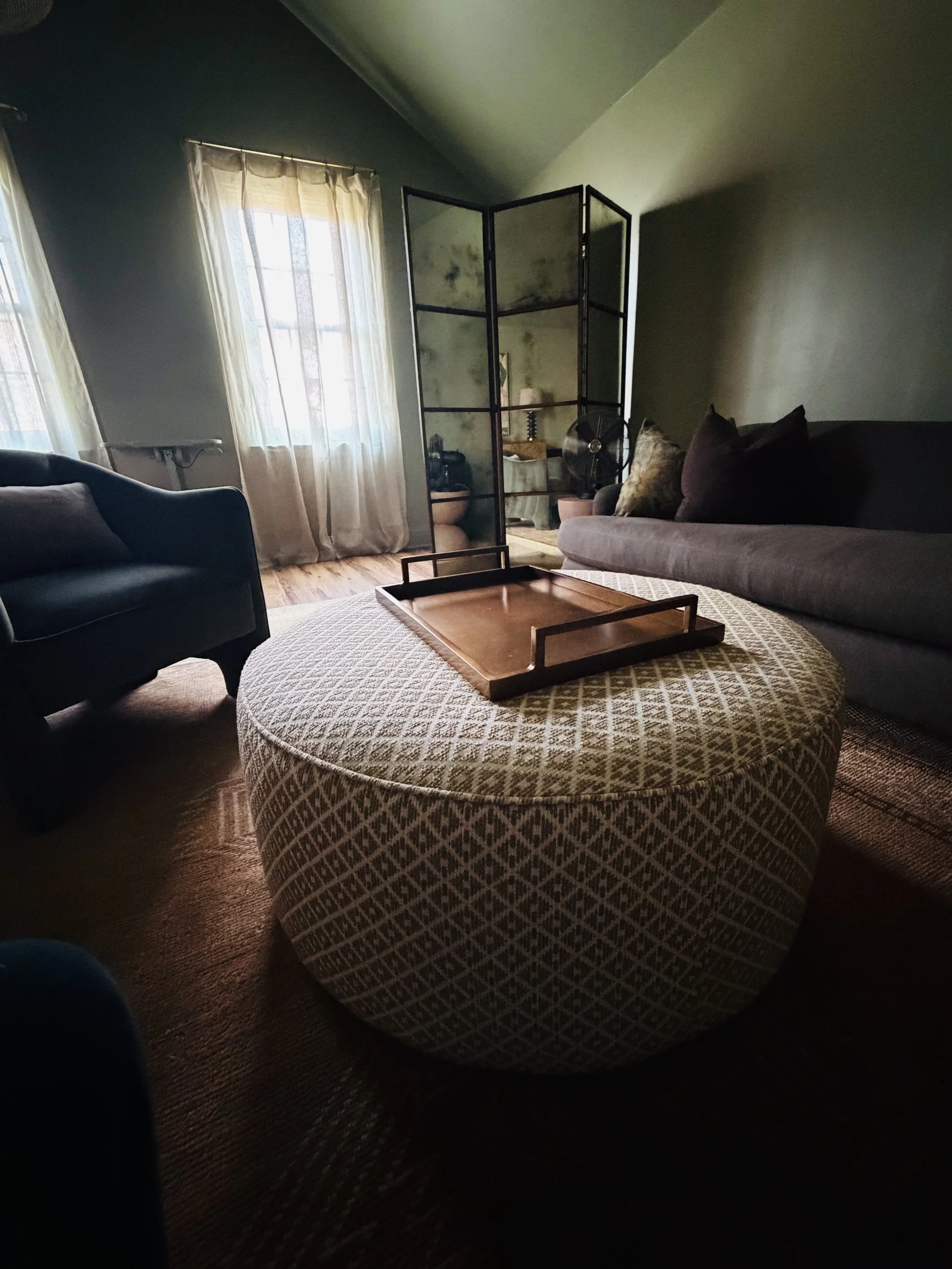 Softly lit sitting room at Althea NOLA with a patterned ottoman, wooden tray, and sofa