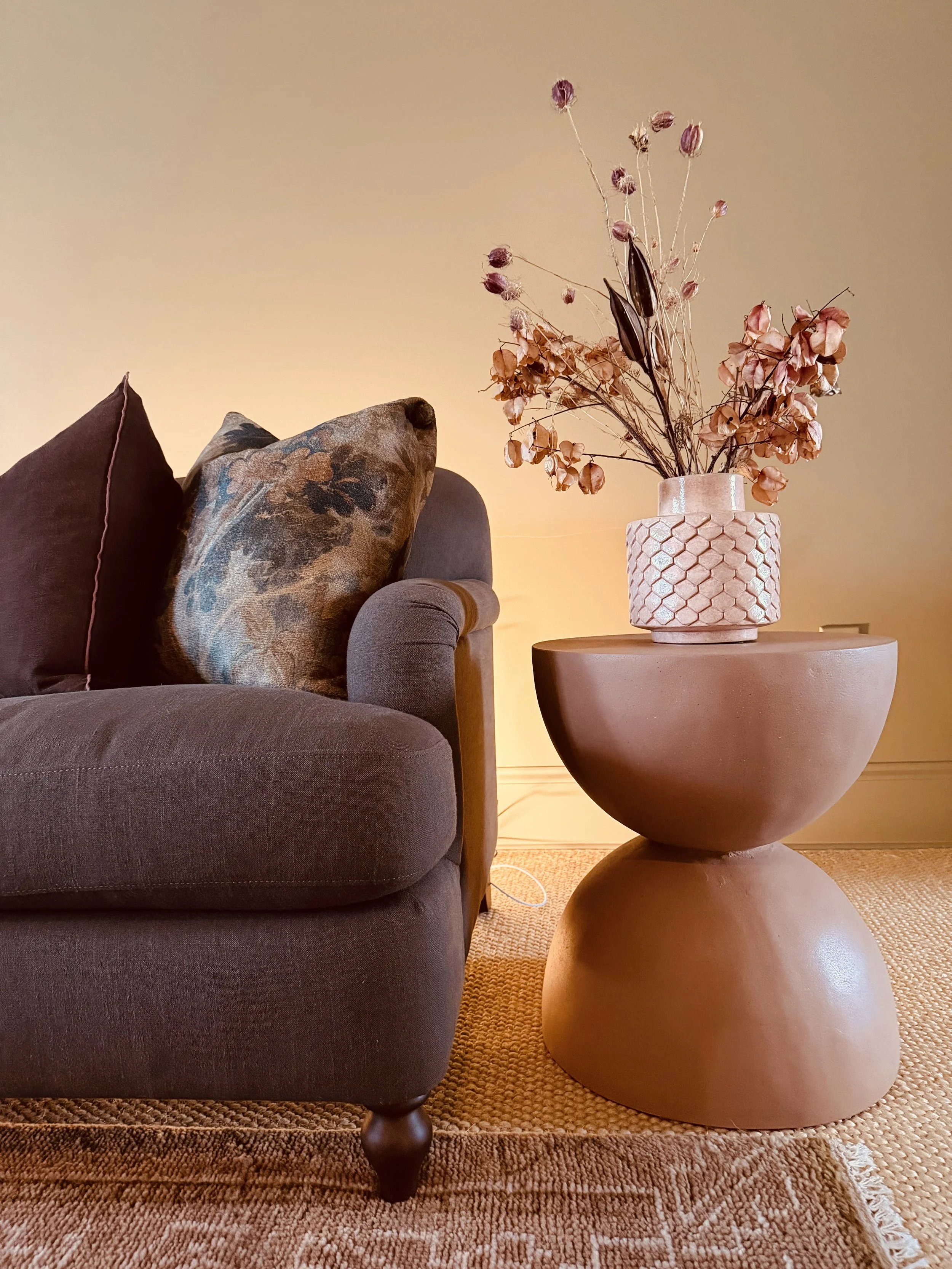 Velvet sofa beside a clay side table with a vase of dried flowers