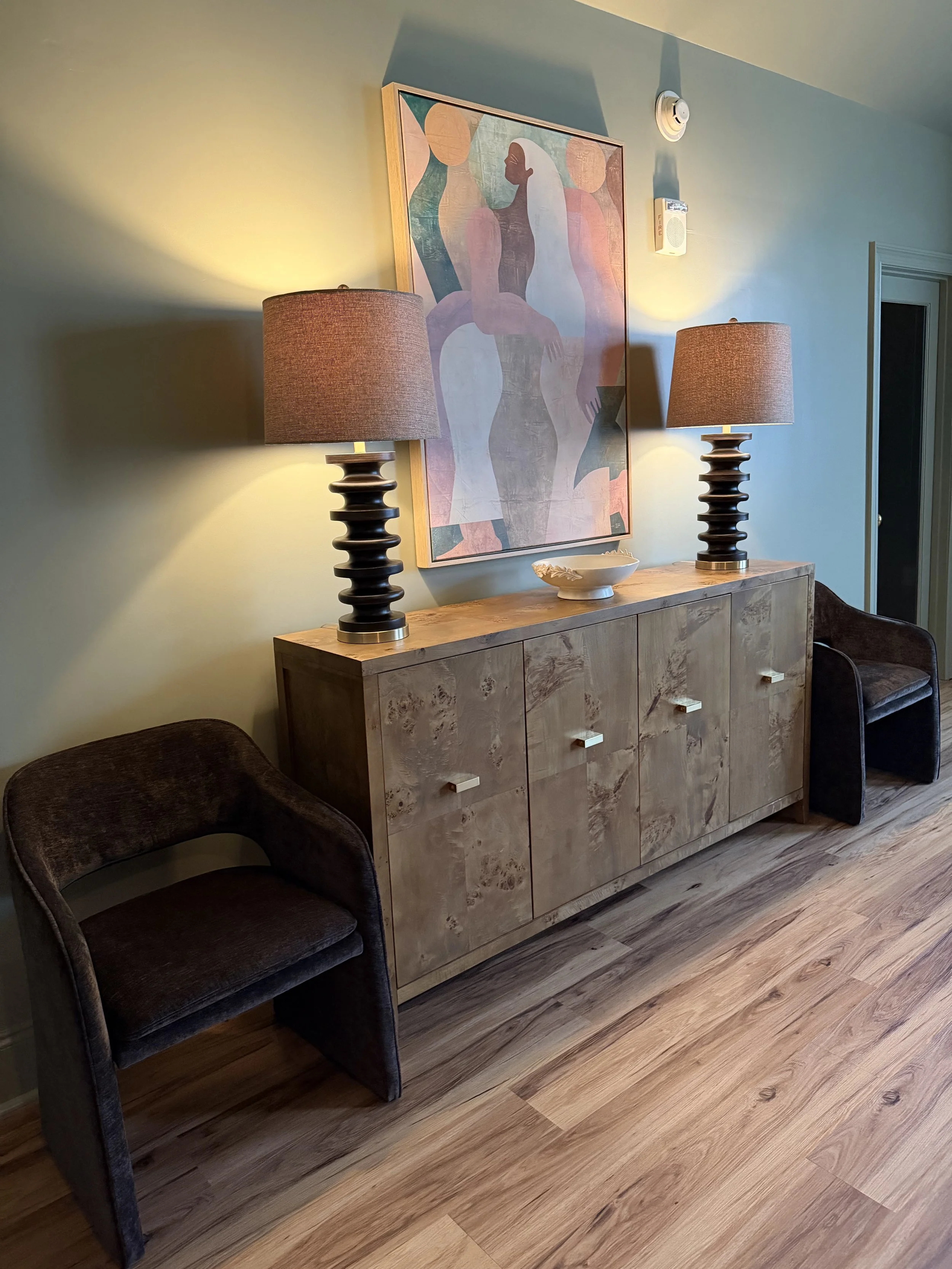 Burl wood credenza with two lamps, a lounge chair, and an abstract painting