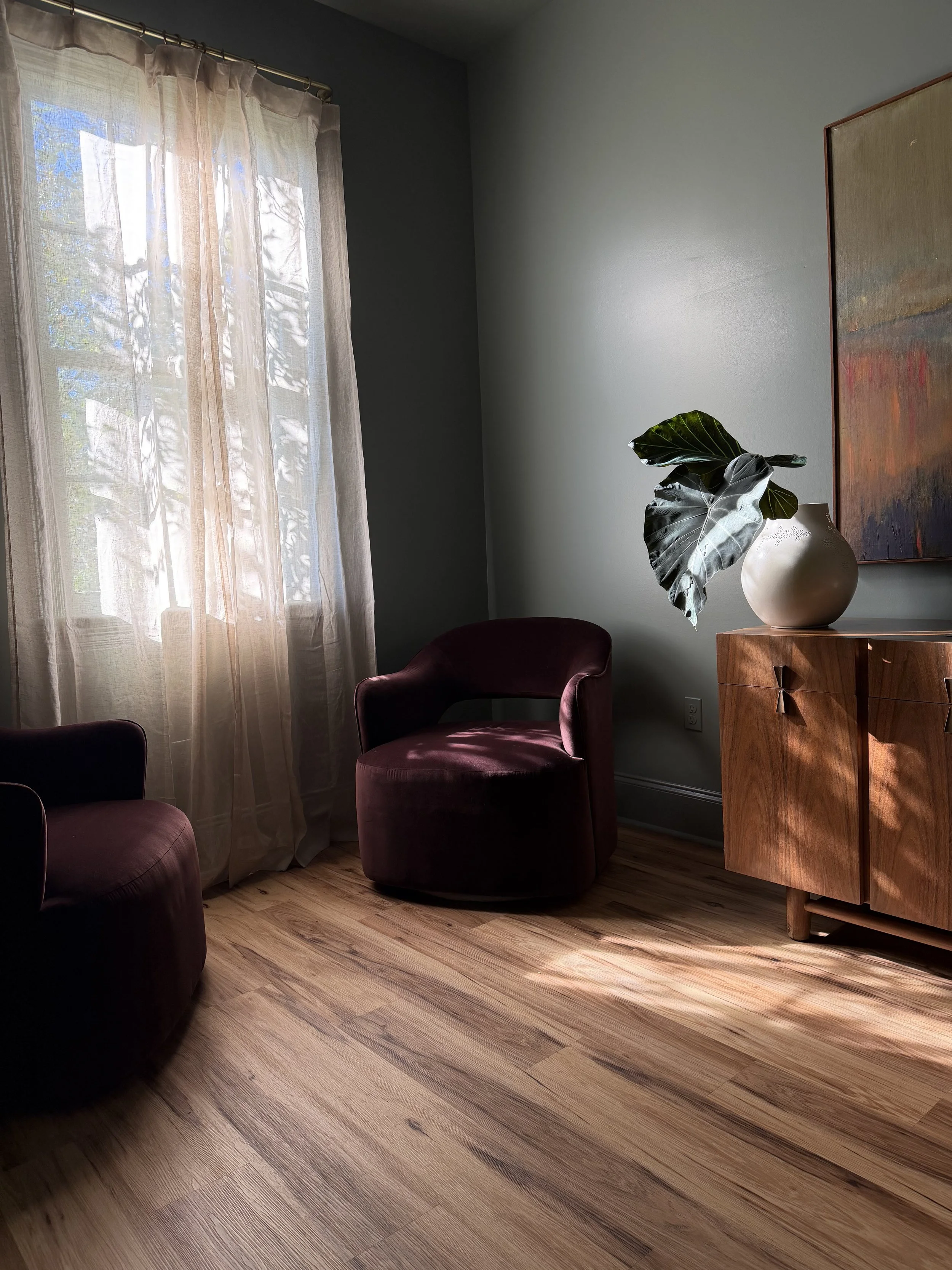 Sunlit room at Althea with plum velvet chairs, sheer curtains, and a leafy plant