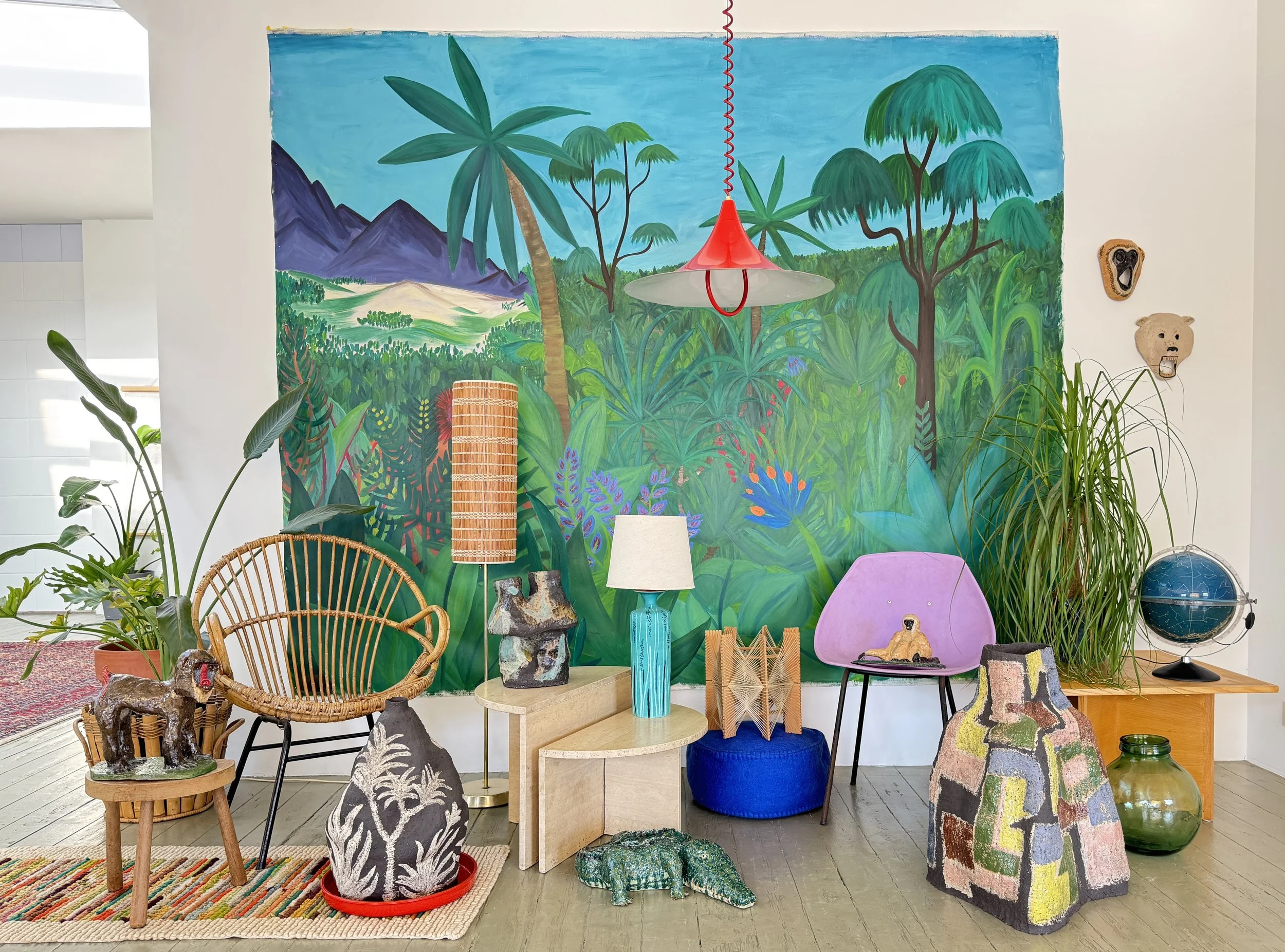 Colorful jungle-themed mural with tropical plants, mountains, and trees as the backdrop of a decorated interior space featuring various chairs, lamps, and decorative items.