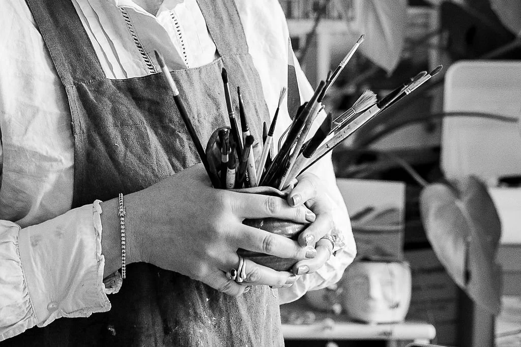 Person holding a container filled with paintbrushes and art tools in a workspace.