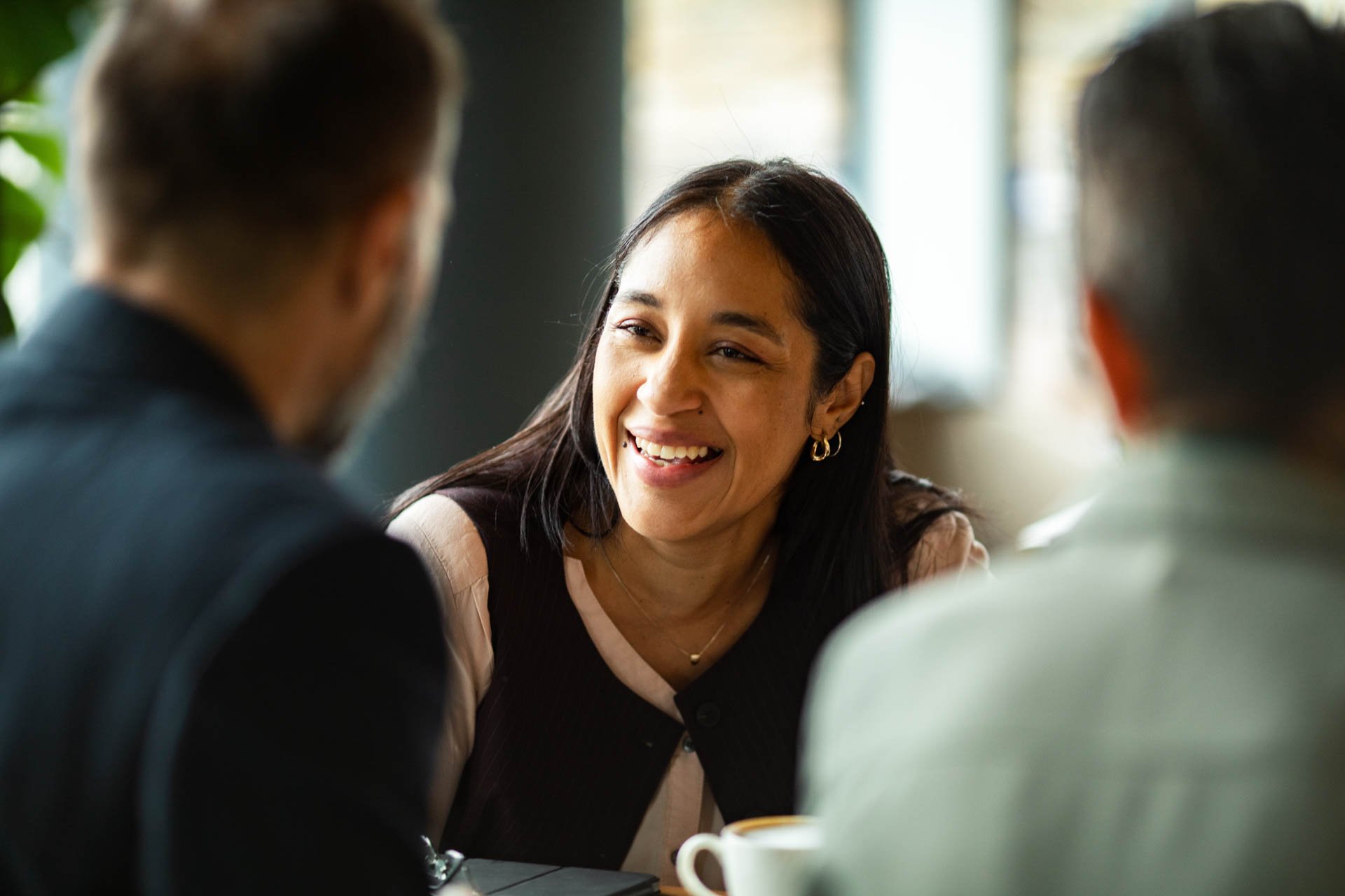 A woman smiling and engaging in conversation with two men in a casual indoor setting.