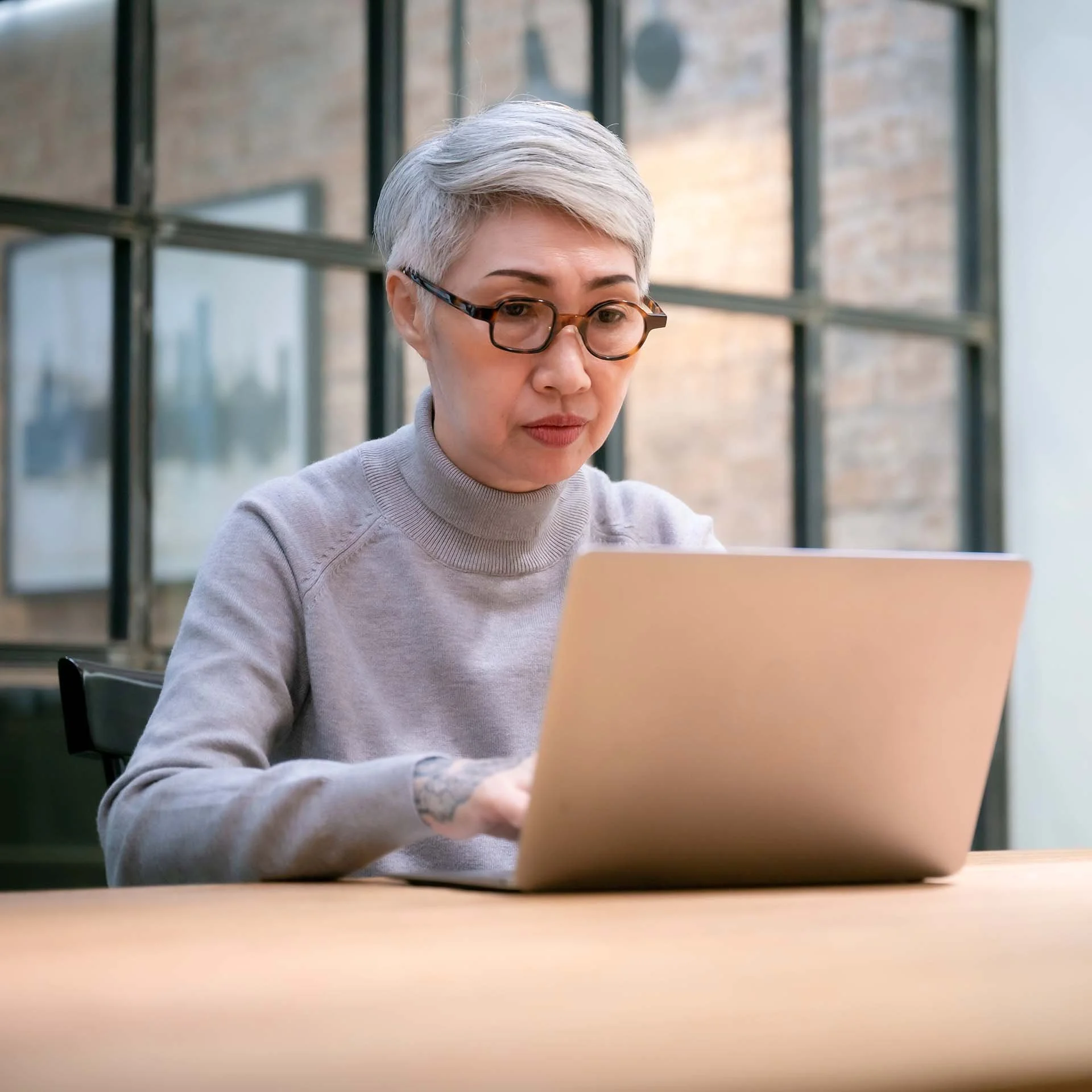 Confident asian woman with short silver hair, but facing her laptop screen with concentrated focus.