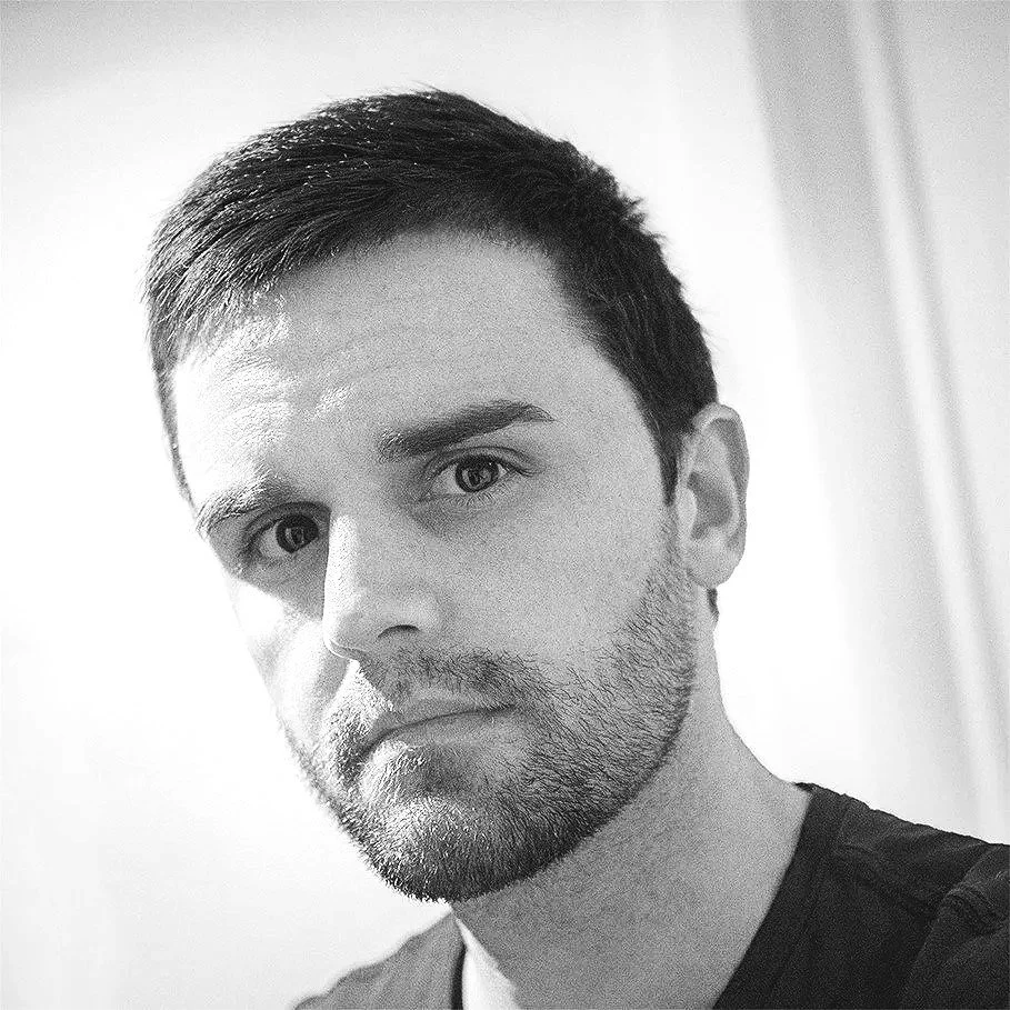 Black and white portrait of a young man with short hair and a beard, looking at the camera.
