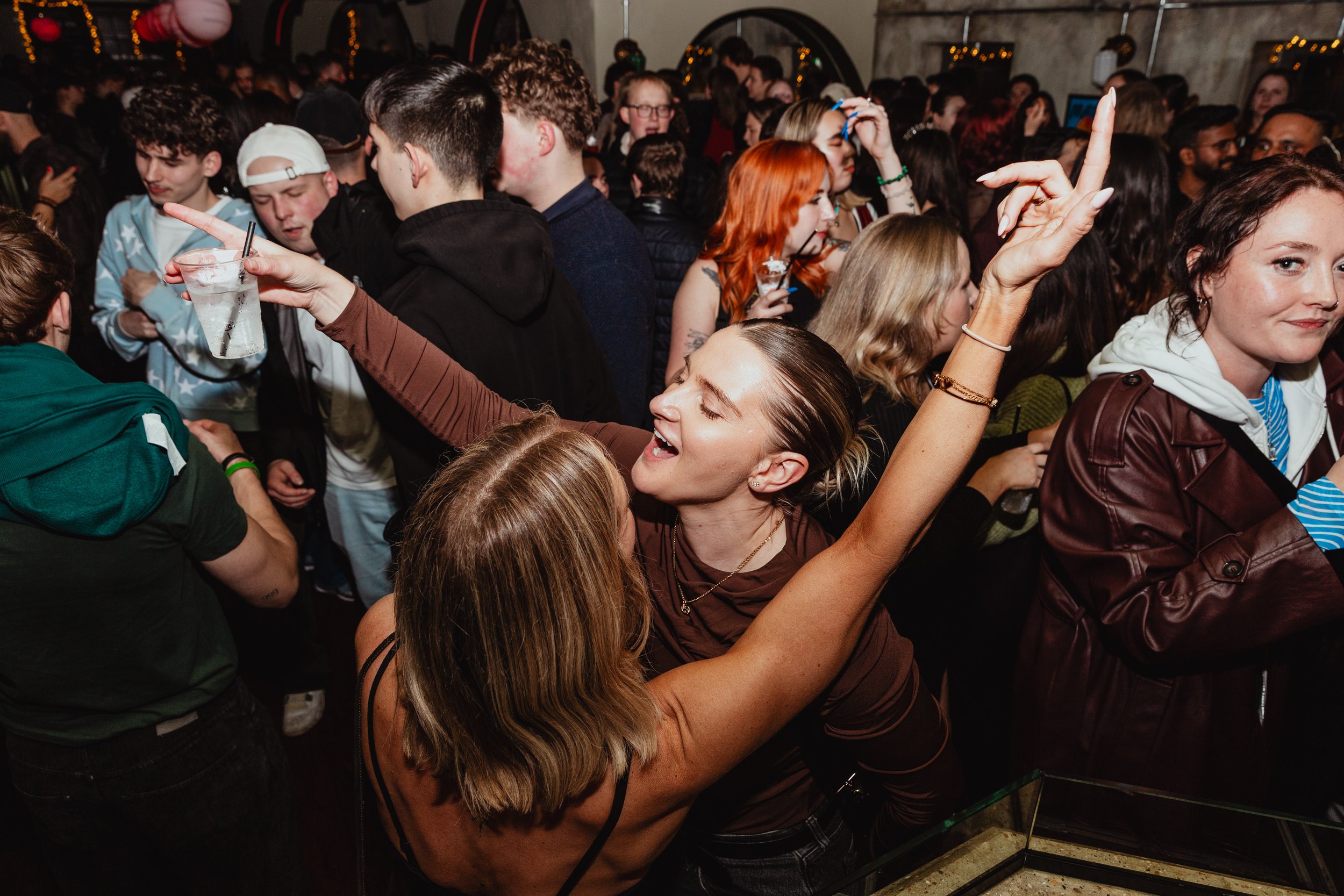 A group of people enjoying a lively party, dancing and smiling in a crowded indoor setting.