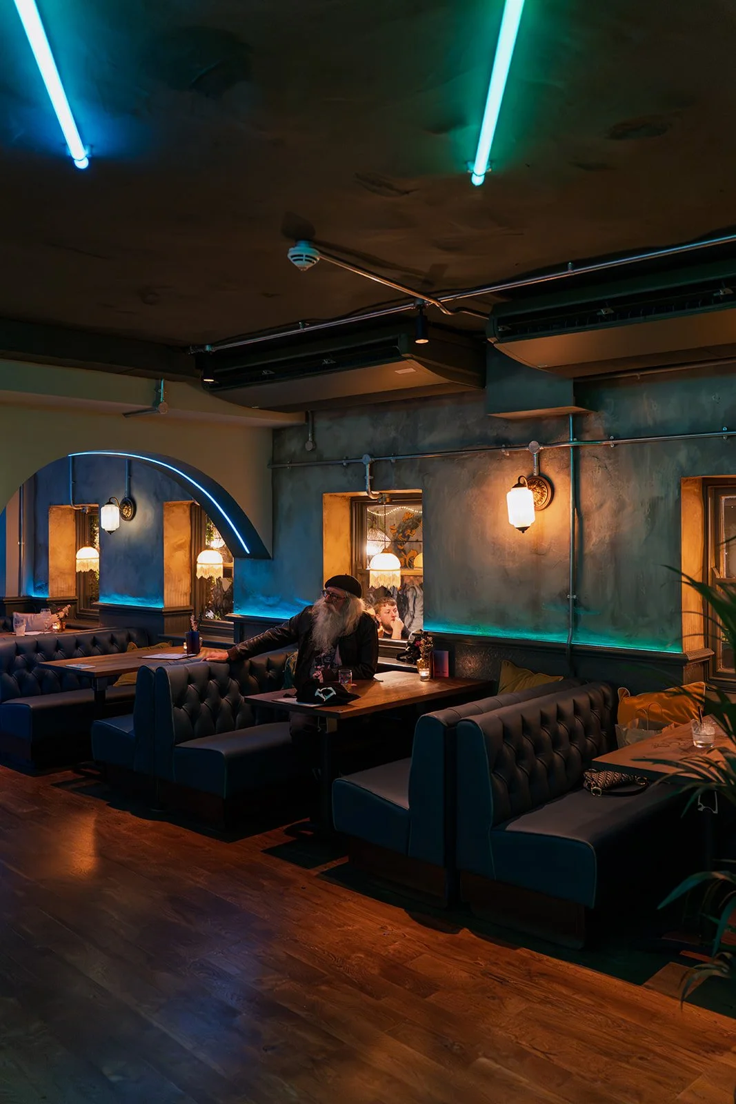 Interior of a dimly lit restaurant or bar with black leather booths, warm lighting, and colorful neon lights on the ceiling.